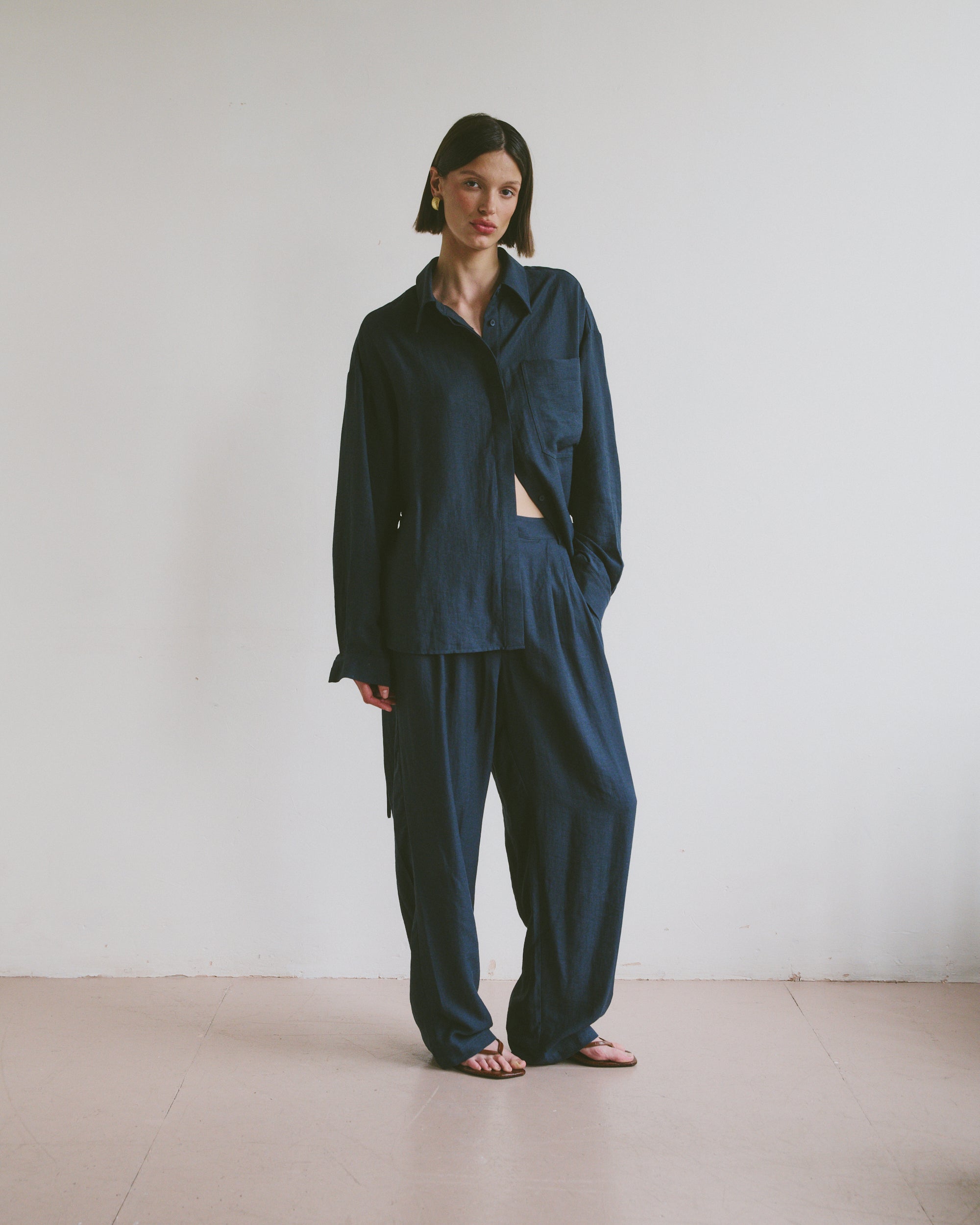 Model wearing a relaxed dark blue outfit standing against a plain white wall.