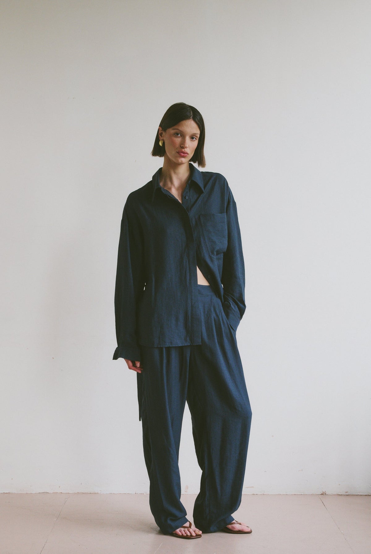 Model wearing a relaxed dark blue outfit standing against a plain white wall.