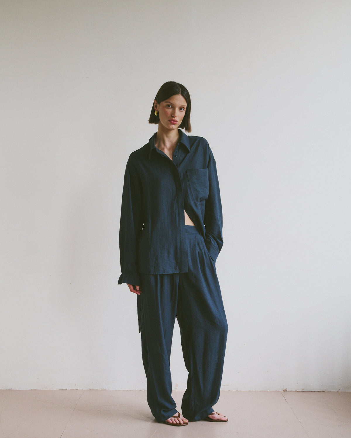 Model wearing a relaxed dark blue outfit standing against a plain white wall.