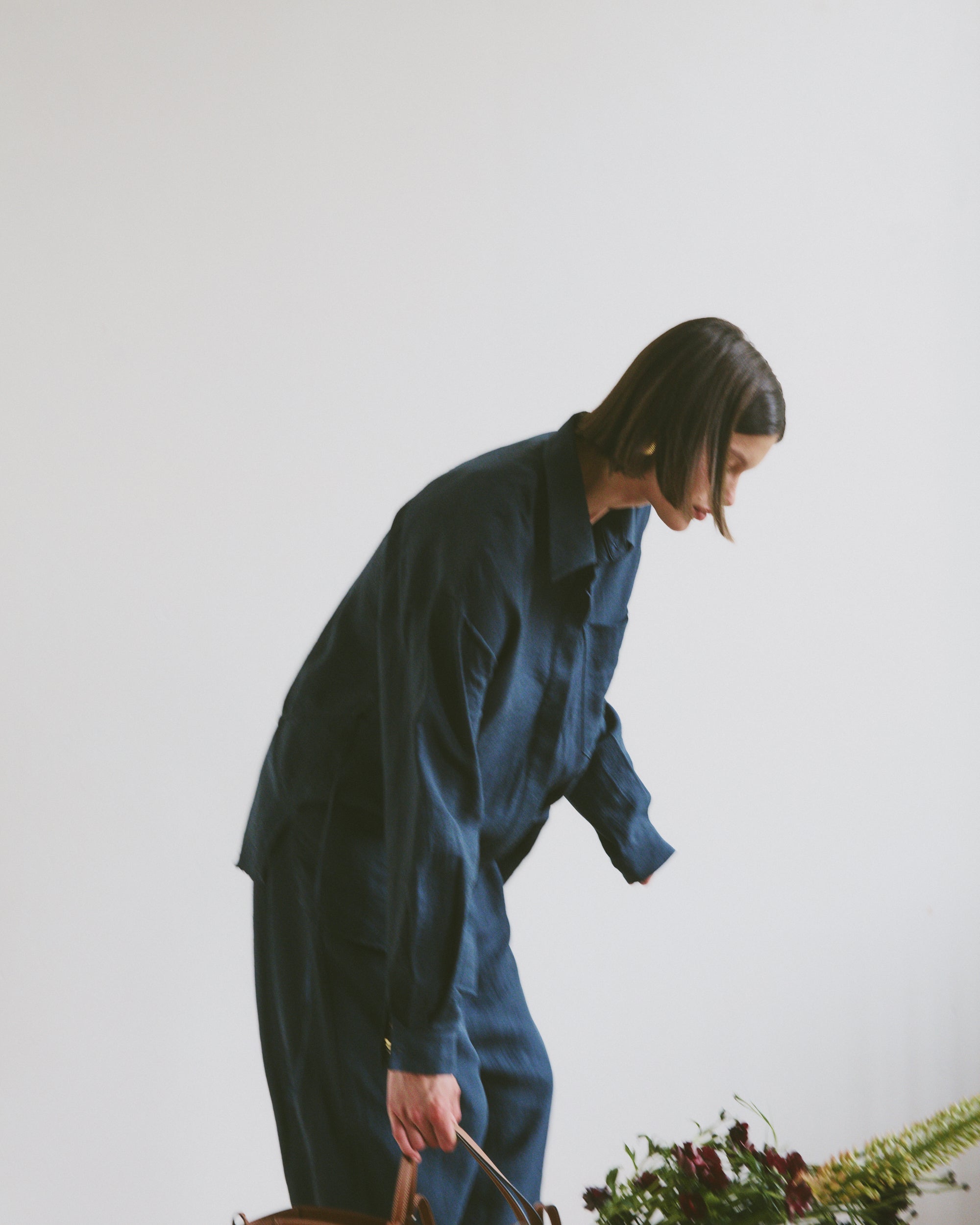 Model wearing a blue outfit holding a woven handbag with flowers and greenery coming out the top