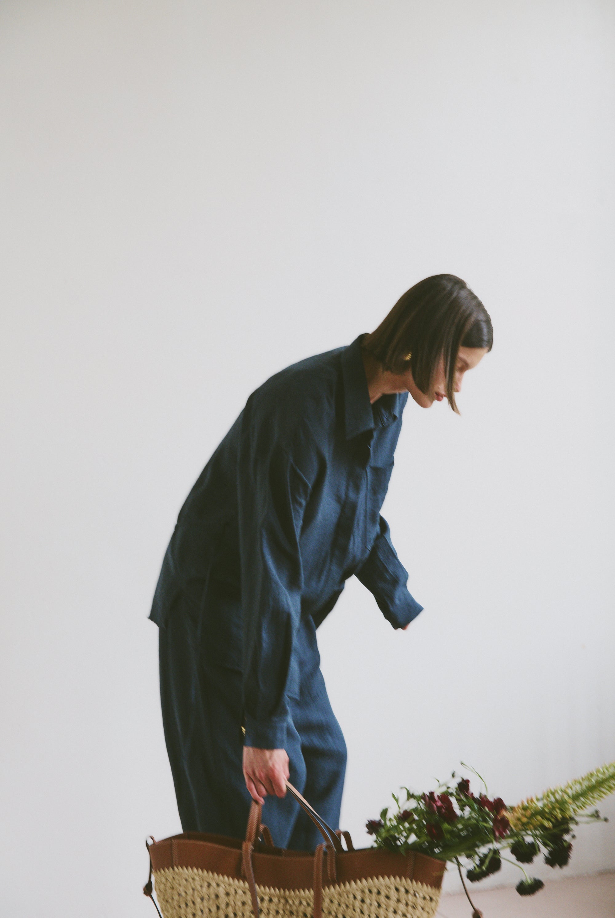 Model wearing a blue outfit holding a woven handbag with flowers and greenery coming out the top