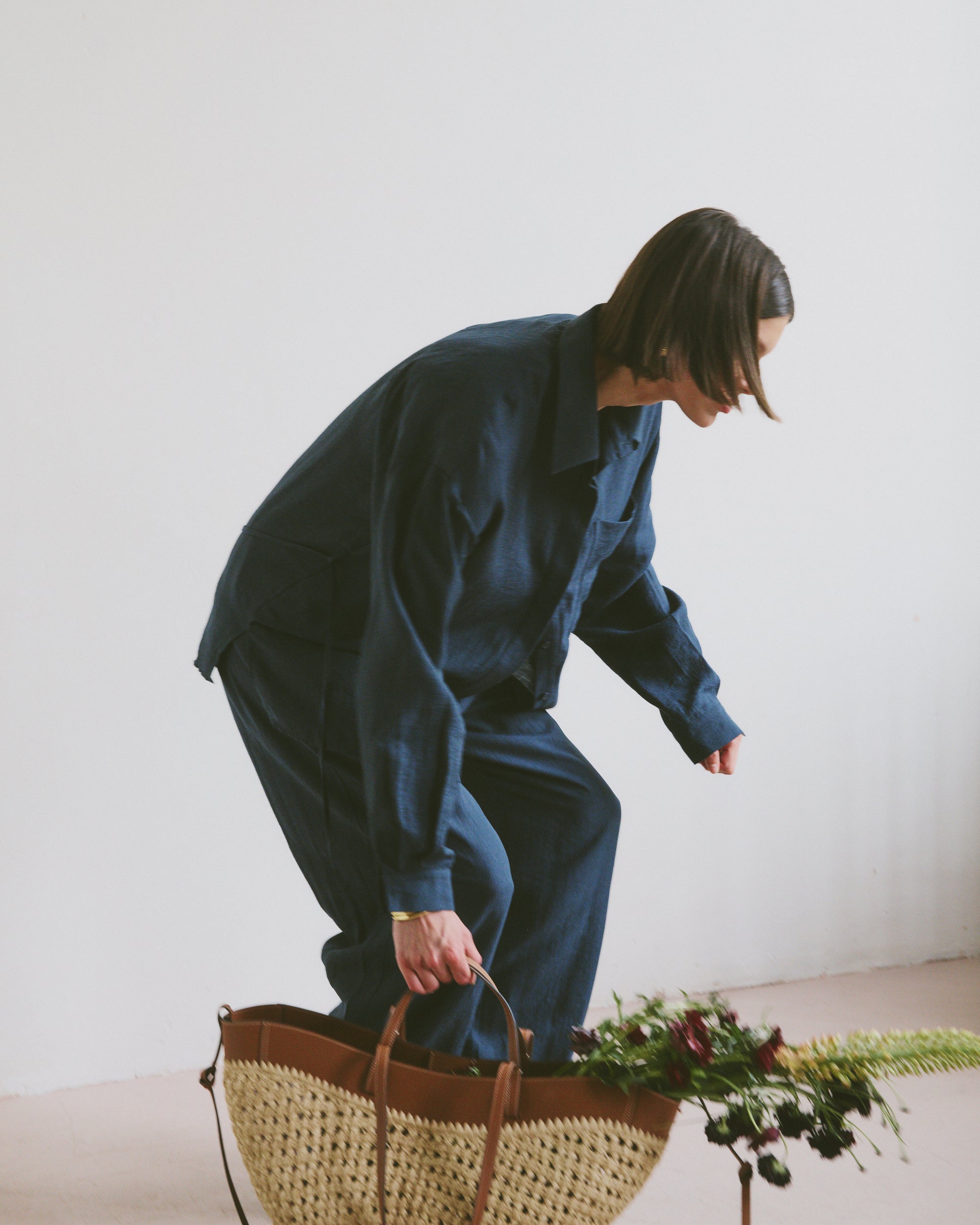 Model in blue outfit with a woven basket and flowers on a light background