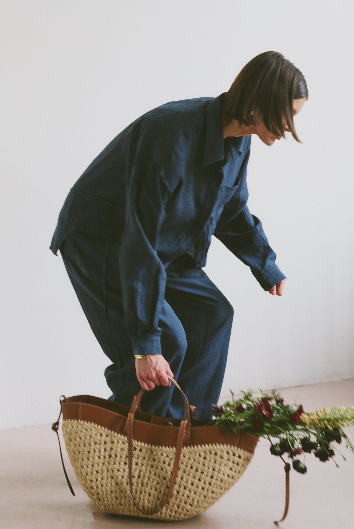 Model in blue outfit with a woven basket and flowers on a light background