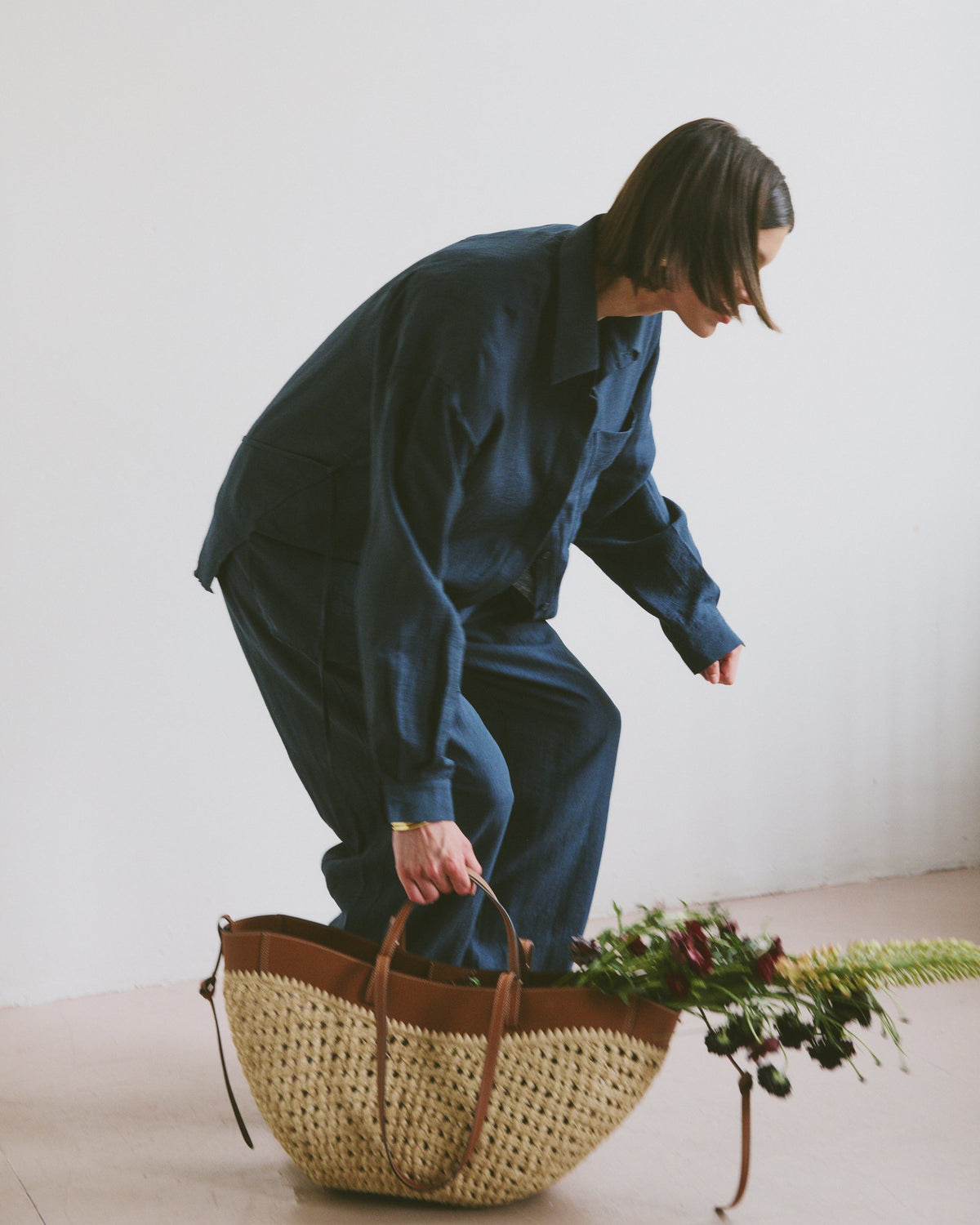Model in blue outfit with a woven basket and flowers on a light background