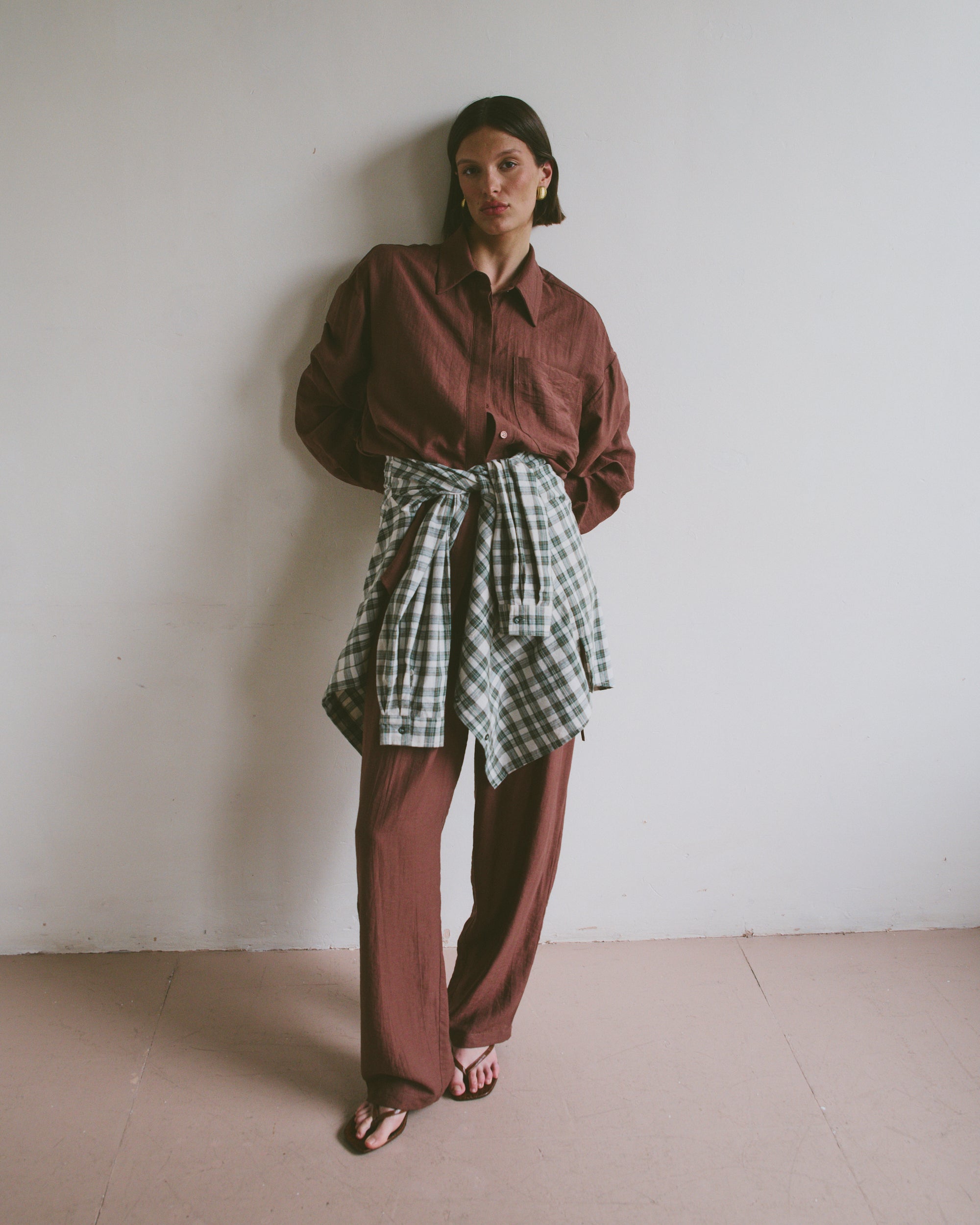 Model wearing a red shirt and plaid skirt against a white wall
