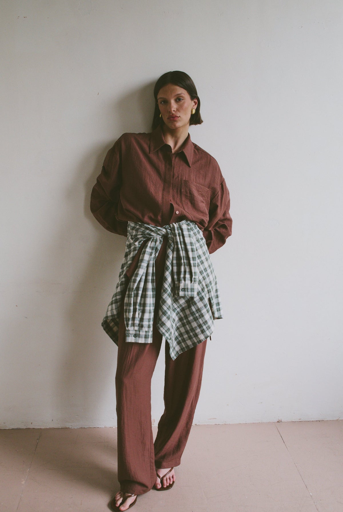 Model wearing a red shirt and plaid skirt against a white wall