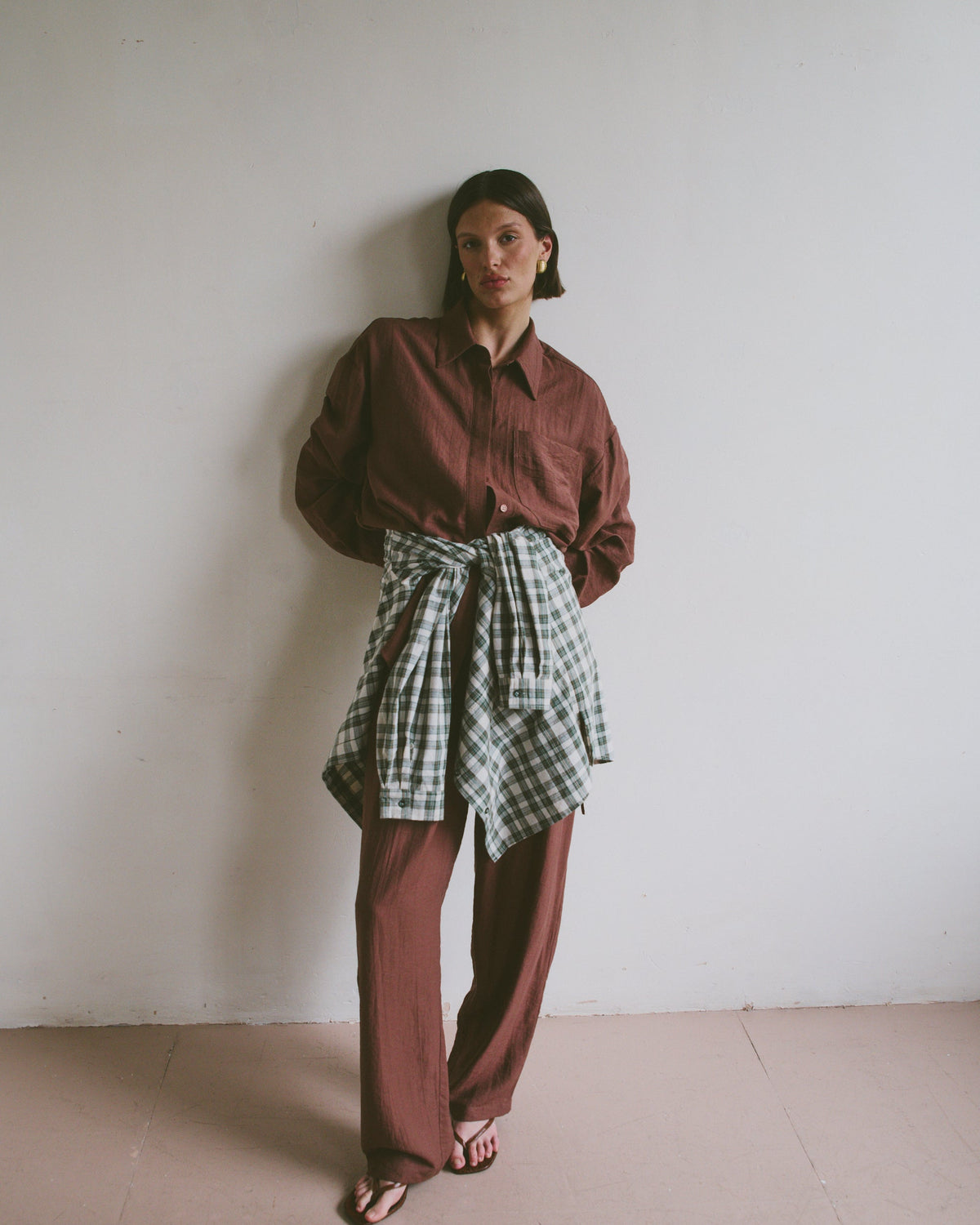 Model wearing a red shirt and plaid skirt against a white wall