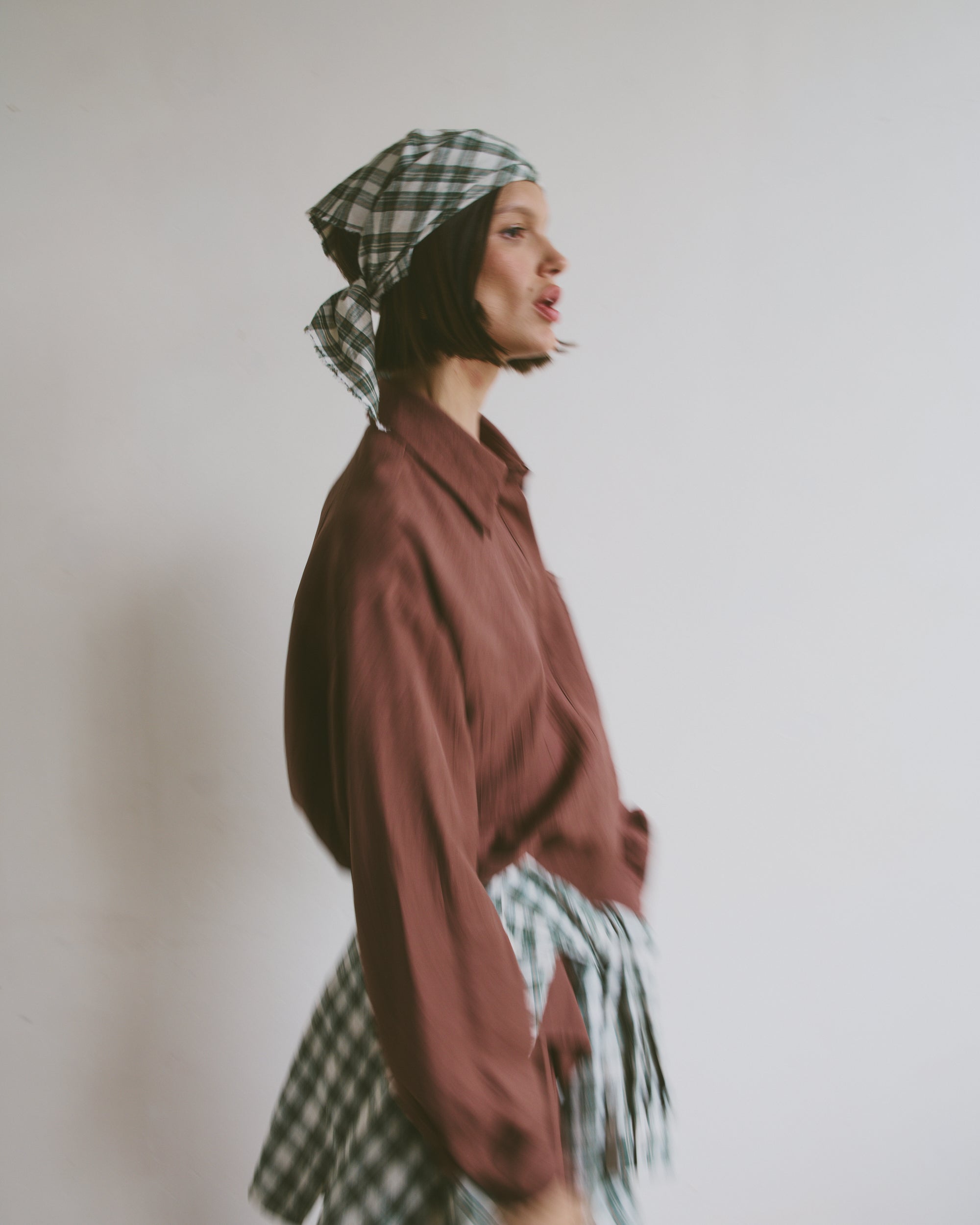 Model wearing a maroon shirt with a plaid headscarf and matching shirt tied around the waist