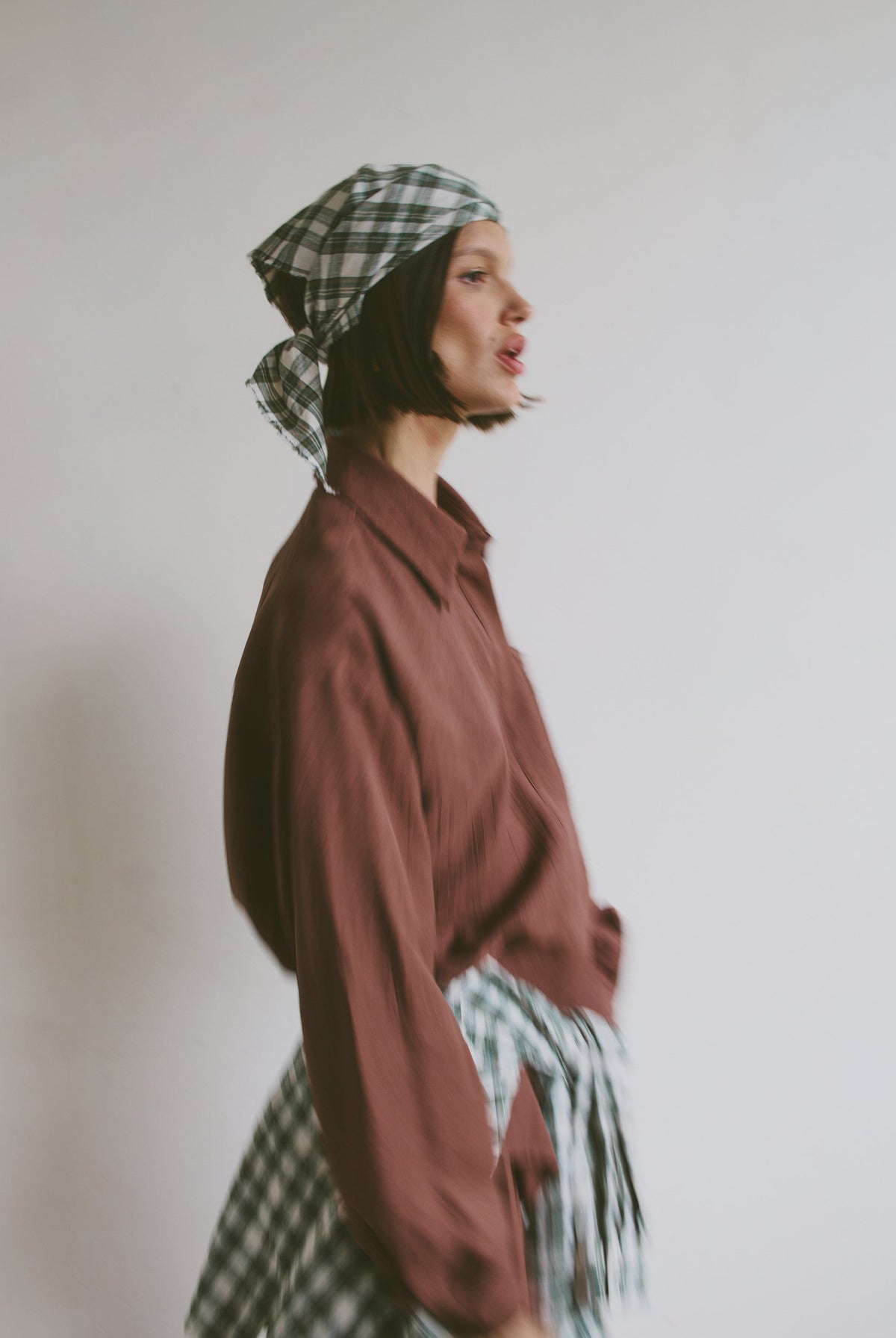 Model wearing a maroon shirt with a plaid headscarf and matching shirt tied around the waist