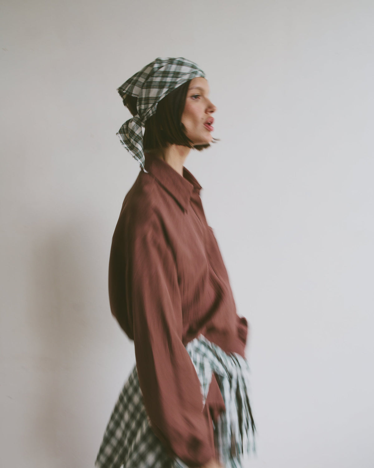 Model wearing a maroon shirt with a plaid headscarf and matching shirt tied around the waist