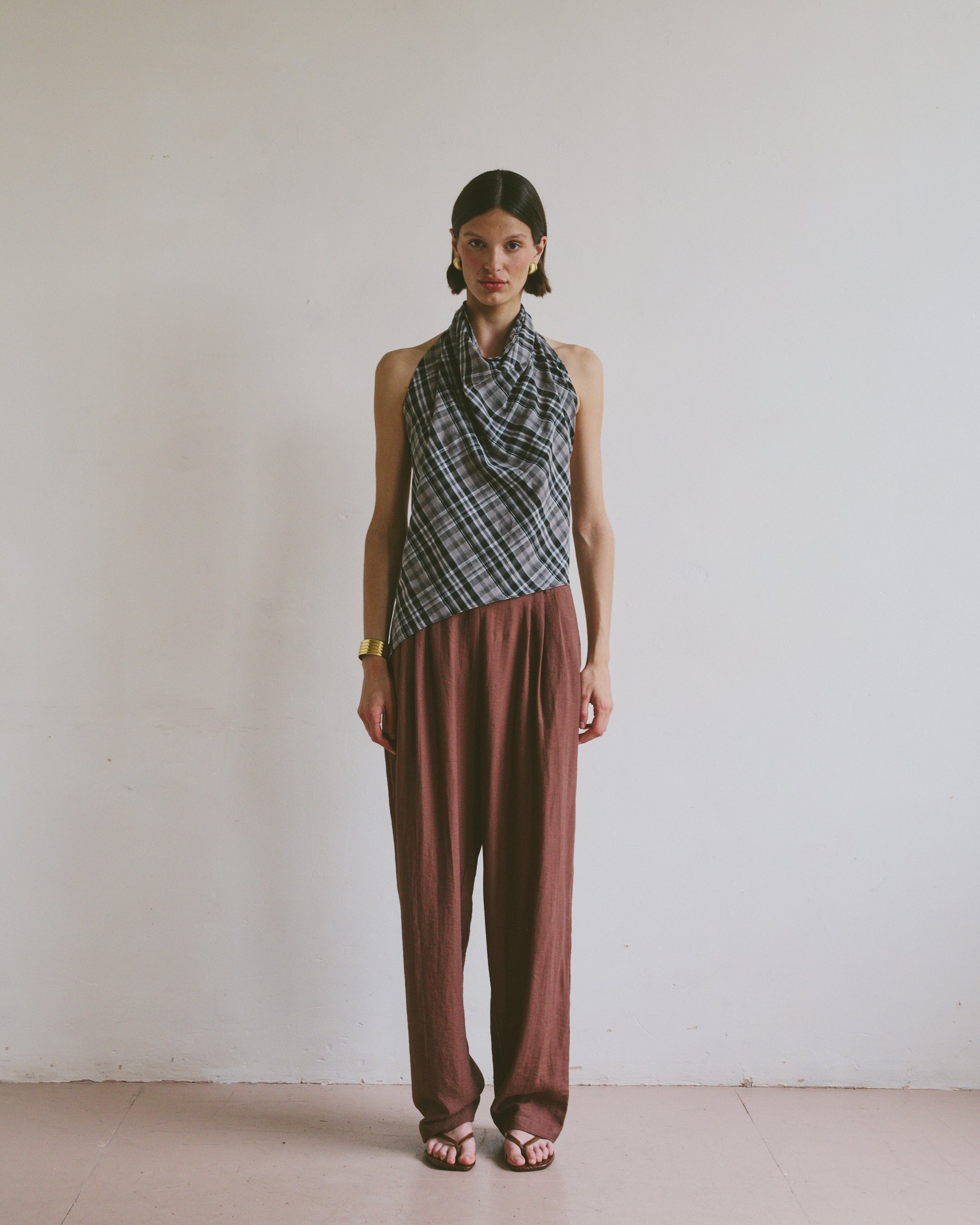 Model wearing a patterned top tied at the neck and maroon brown trousers against a plain background