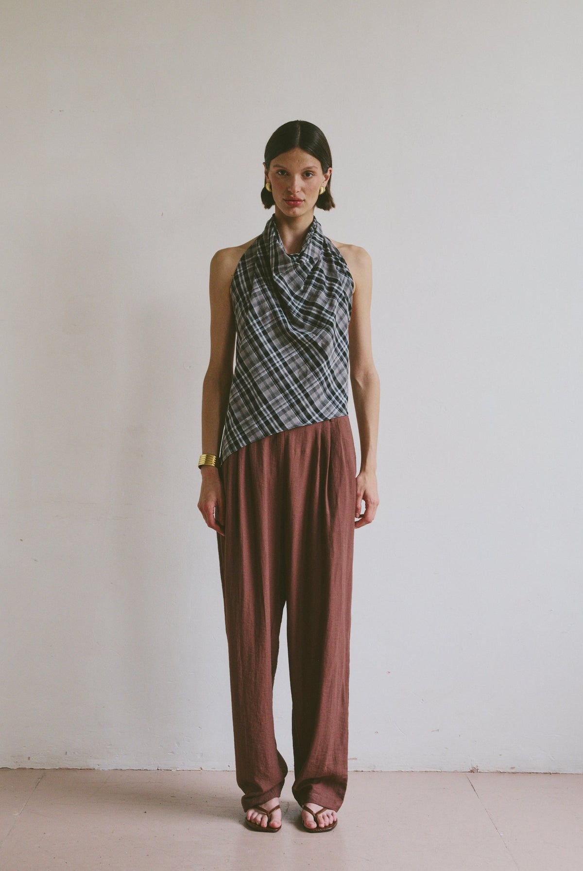 Model wearing a patterned top tied at the neck and maroon brown trousers against a plain background