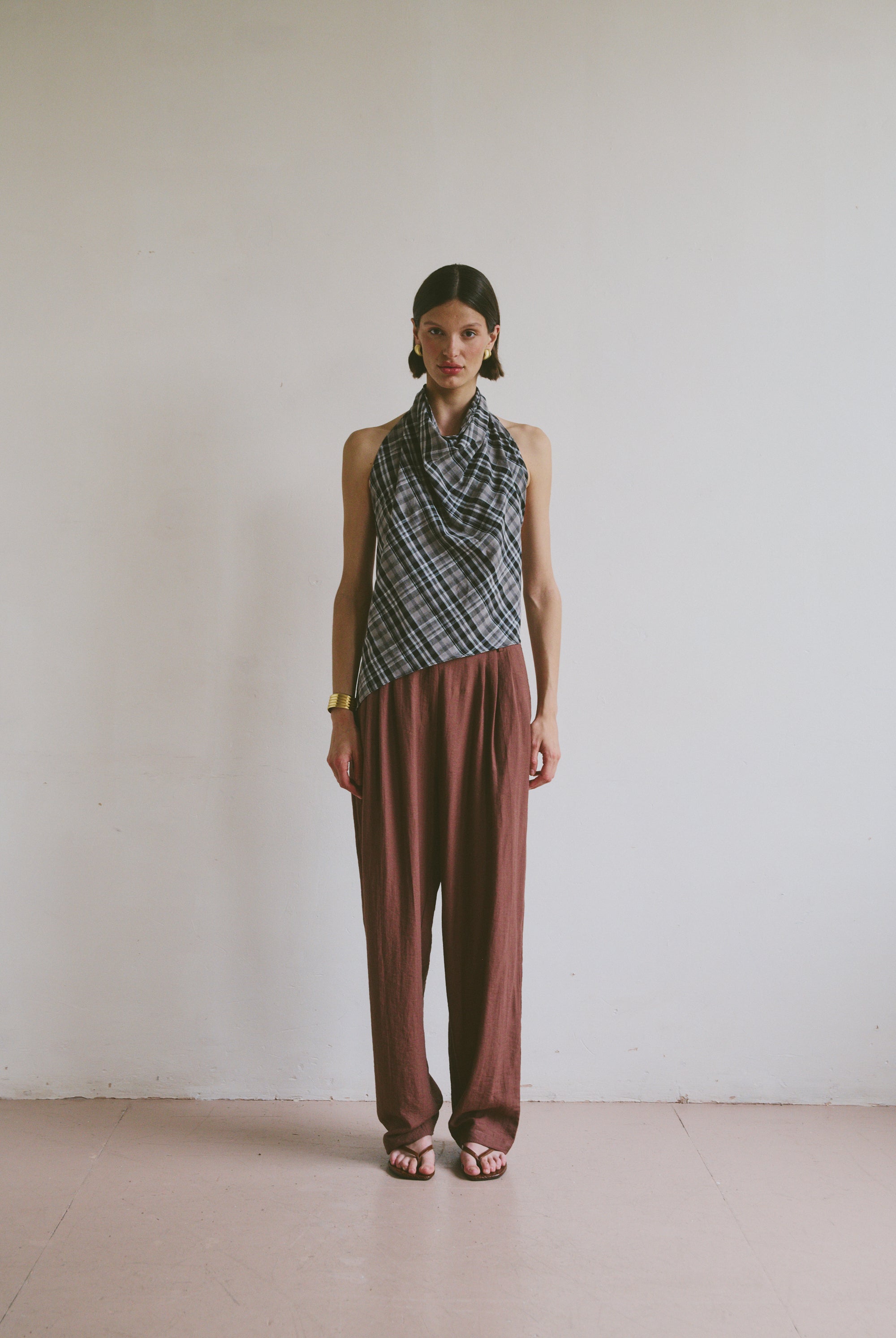 Model wearing a patterned top tied at the neck and maroon brown trousers against a plain background