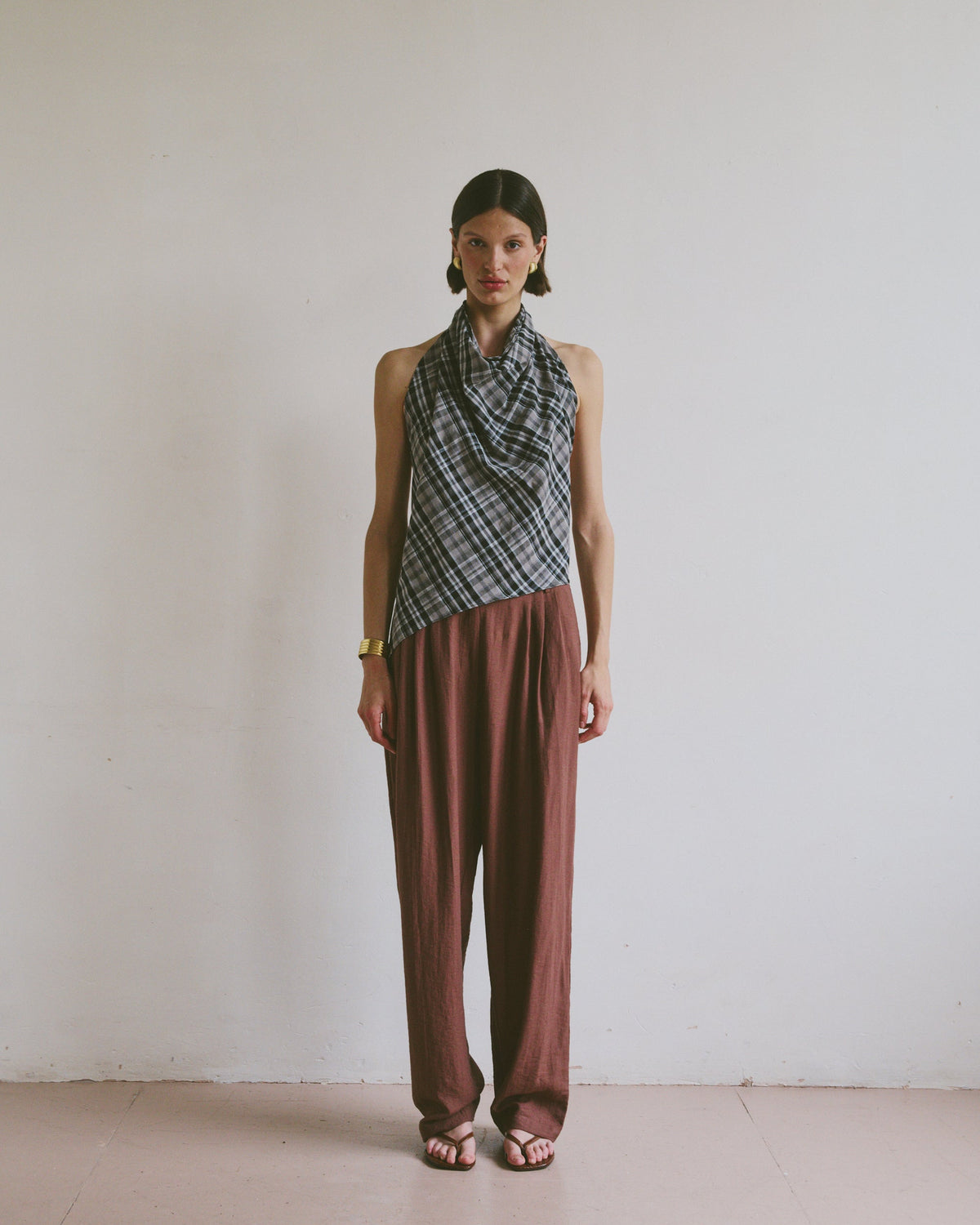 Model wearing a patterned top tied at the neck and maroon brown trousers against a plain background