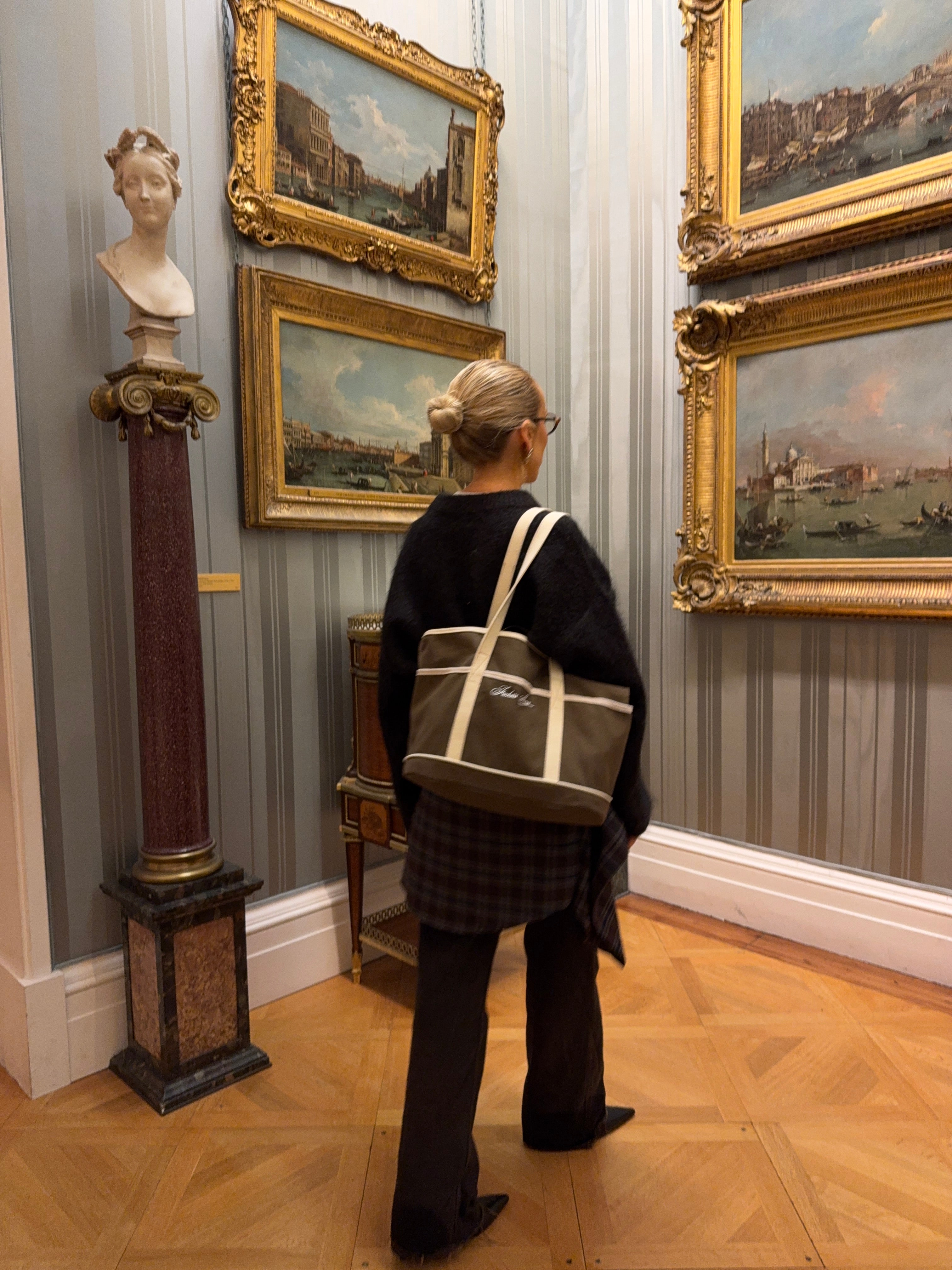 Woman in an art museum wearing all black and carrying a olive brown and cream bag