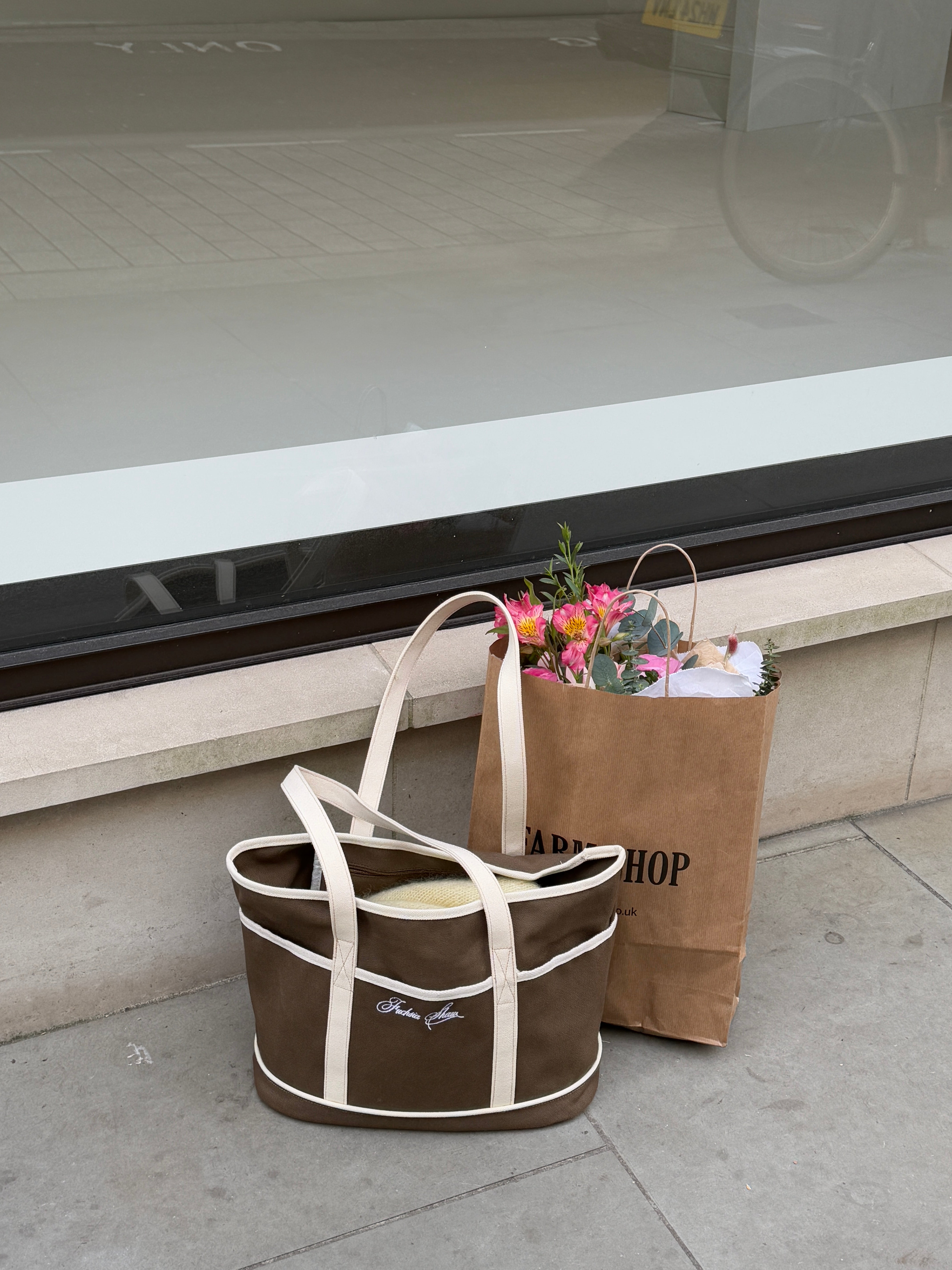 Brown and white tote bag next to a paper bag full of flowers