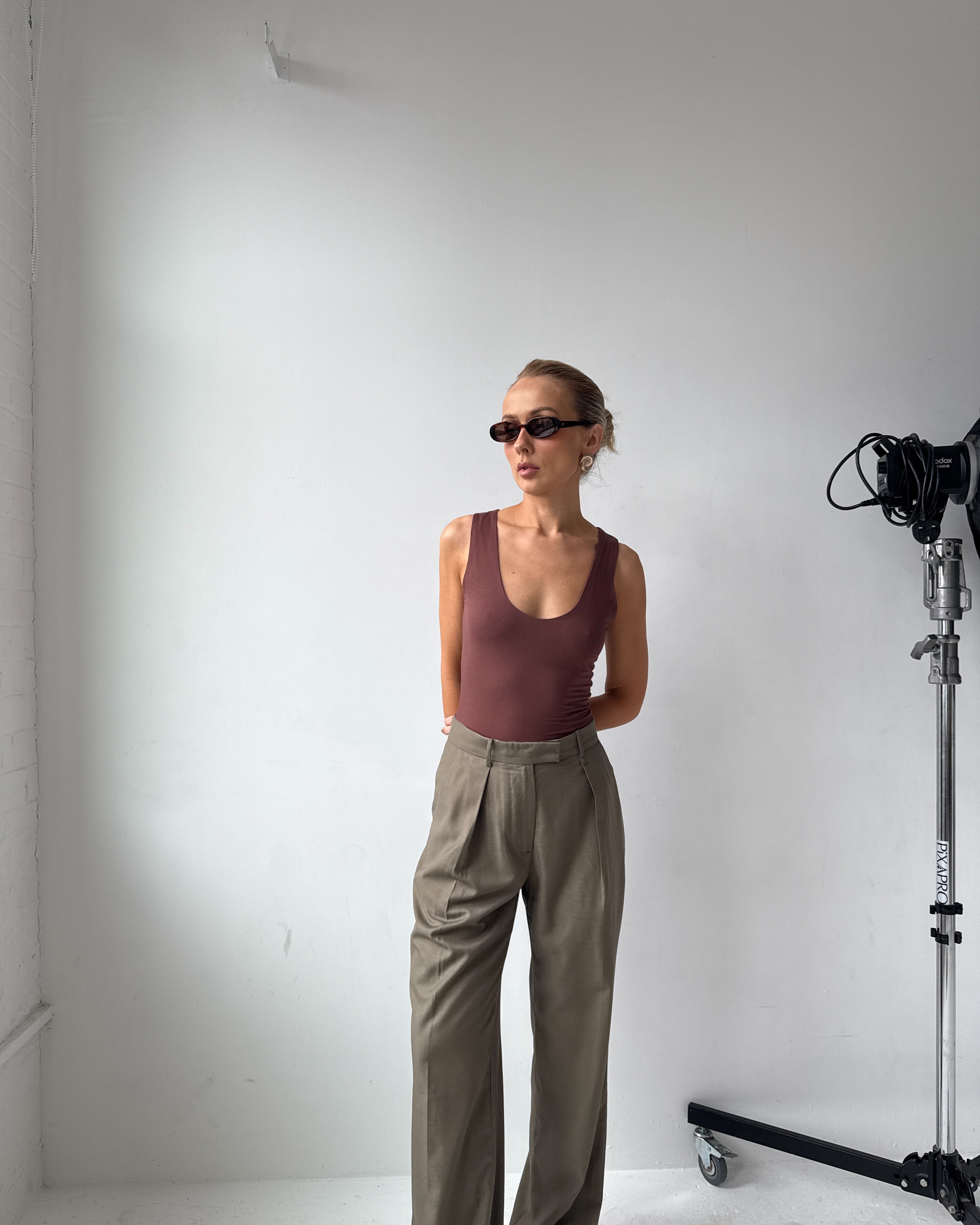 Model wearing a brown tank top, beige trousers and sunglasses in a studio setting with camera equipment
