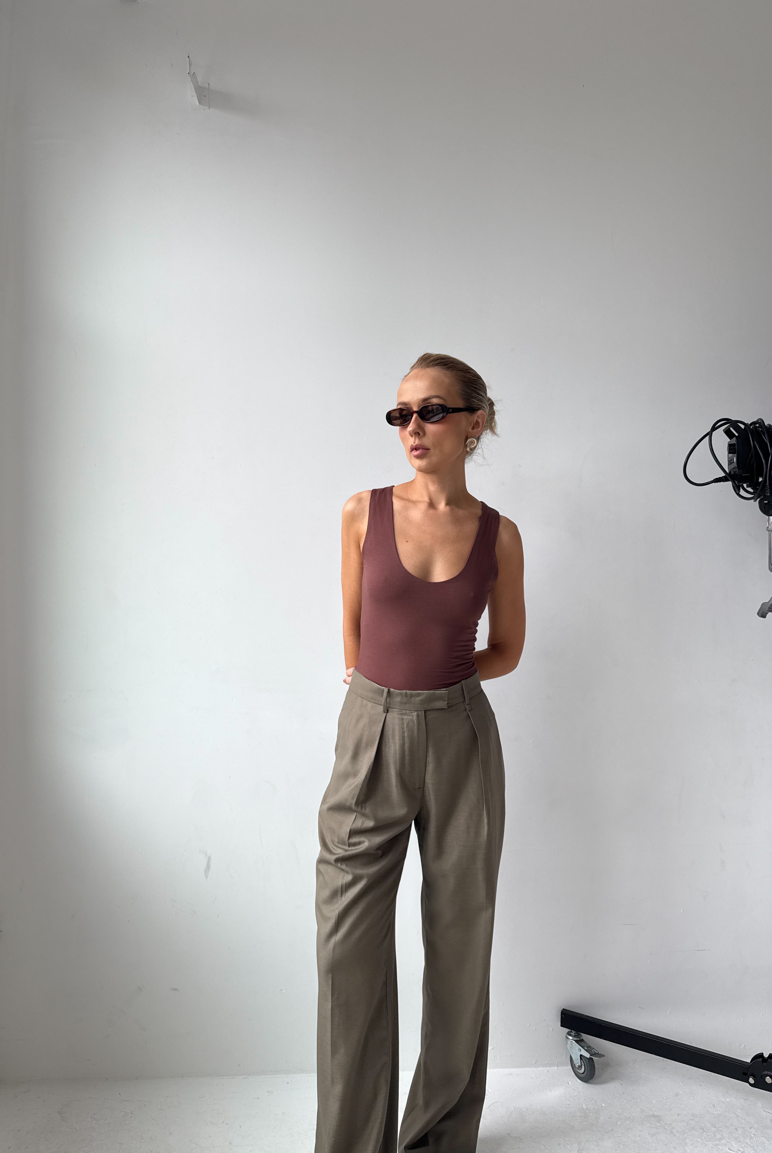 Model wearing a brown tank top, beige trousers and sunglasses in a studio setting with camera equipment