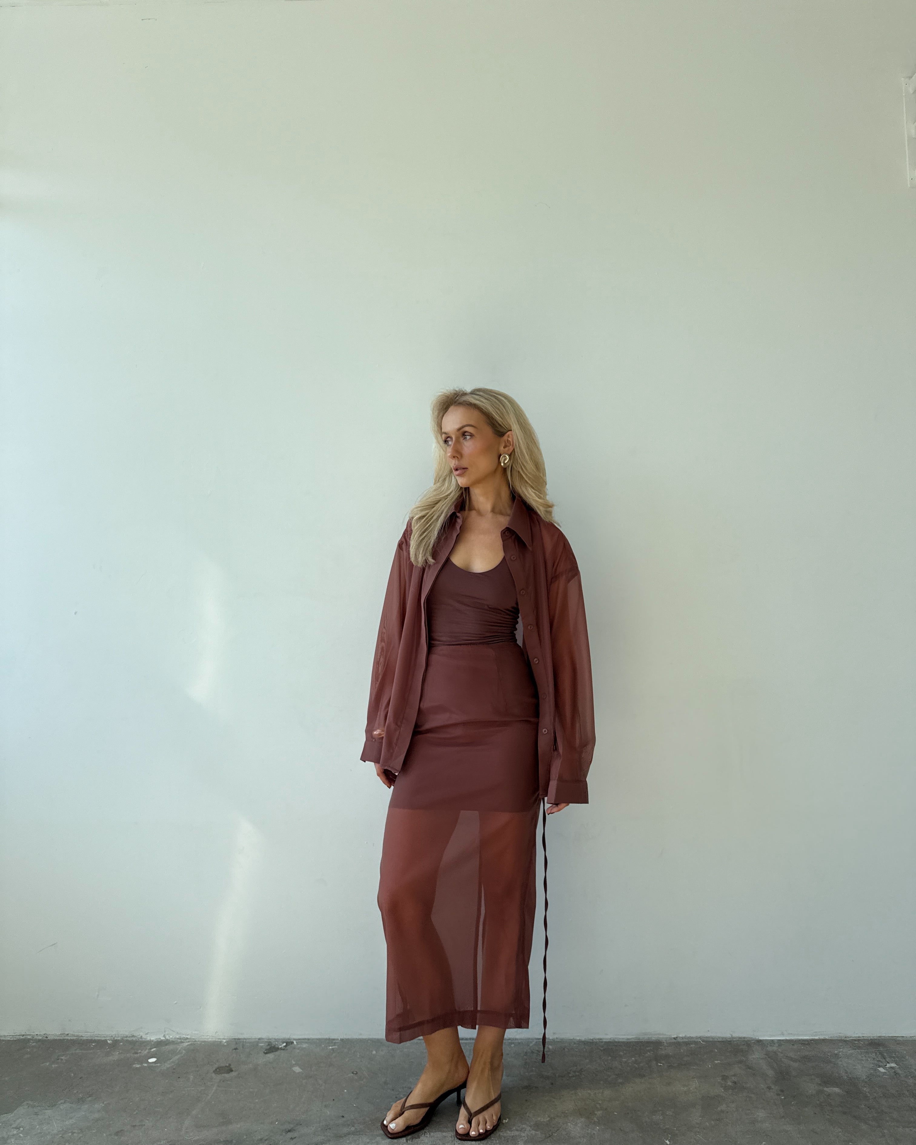 Model wearing a maroon outfit standing against a white wall