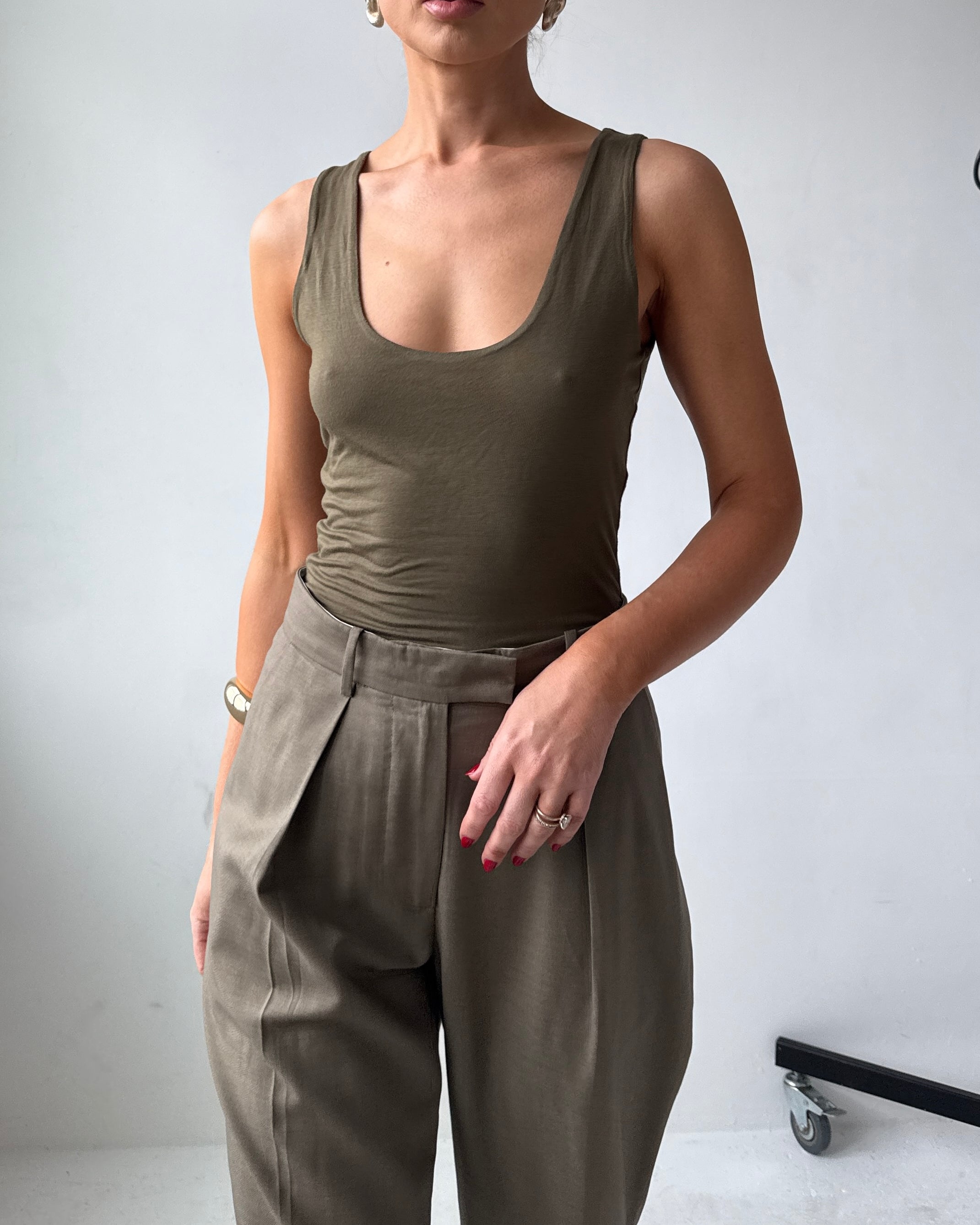 Model wearing a fitted olive green tank top and high-waisted pants against a plain background