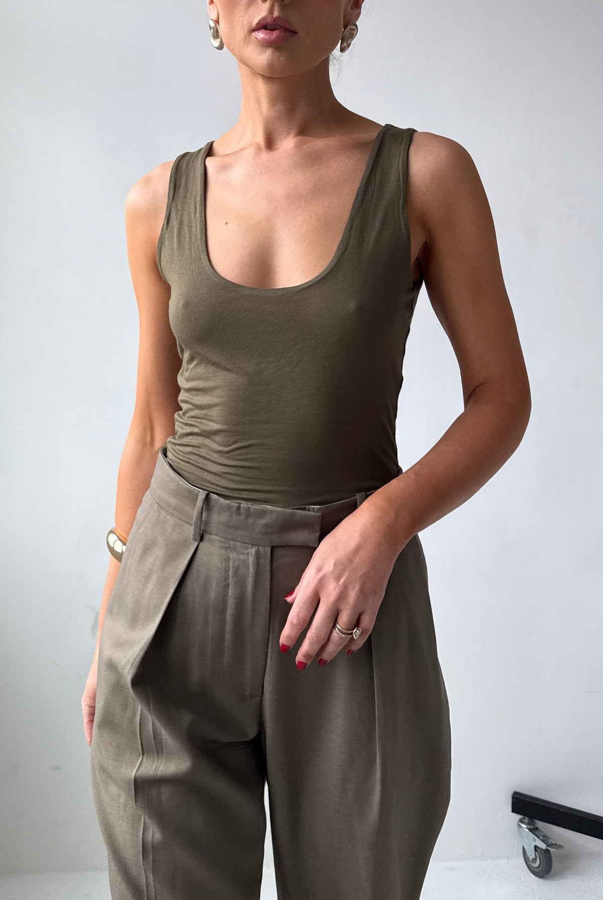 Model wearing a fitted olive green tank top and high-waisted pants against a plain background
