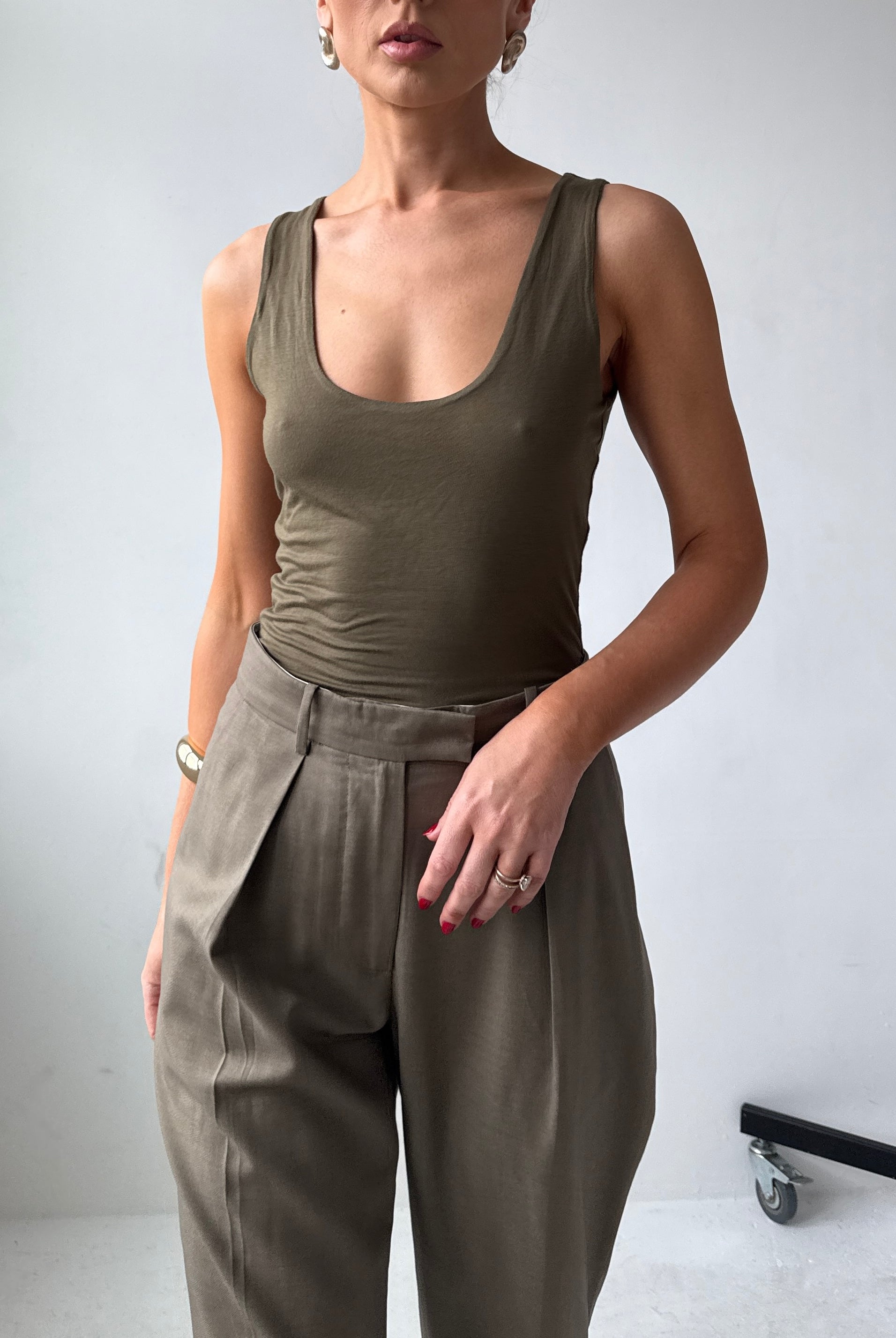 Model wearing a fitted olive green tank top and high-waisted pants against a plain background