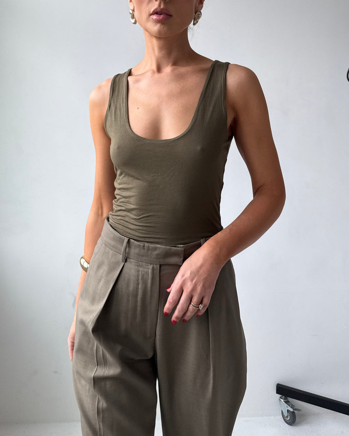 Model wearing a fitted olive green tank top and high-waisted pants against a plain background