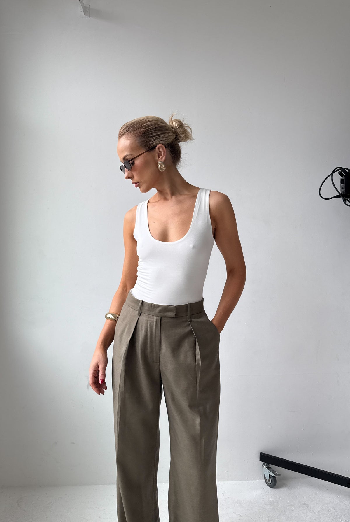 Model in a white tank top and grey trousers standing in a studio setting