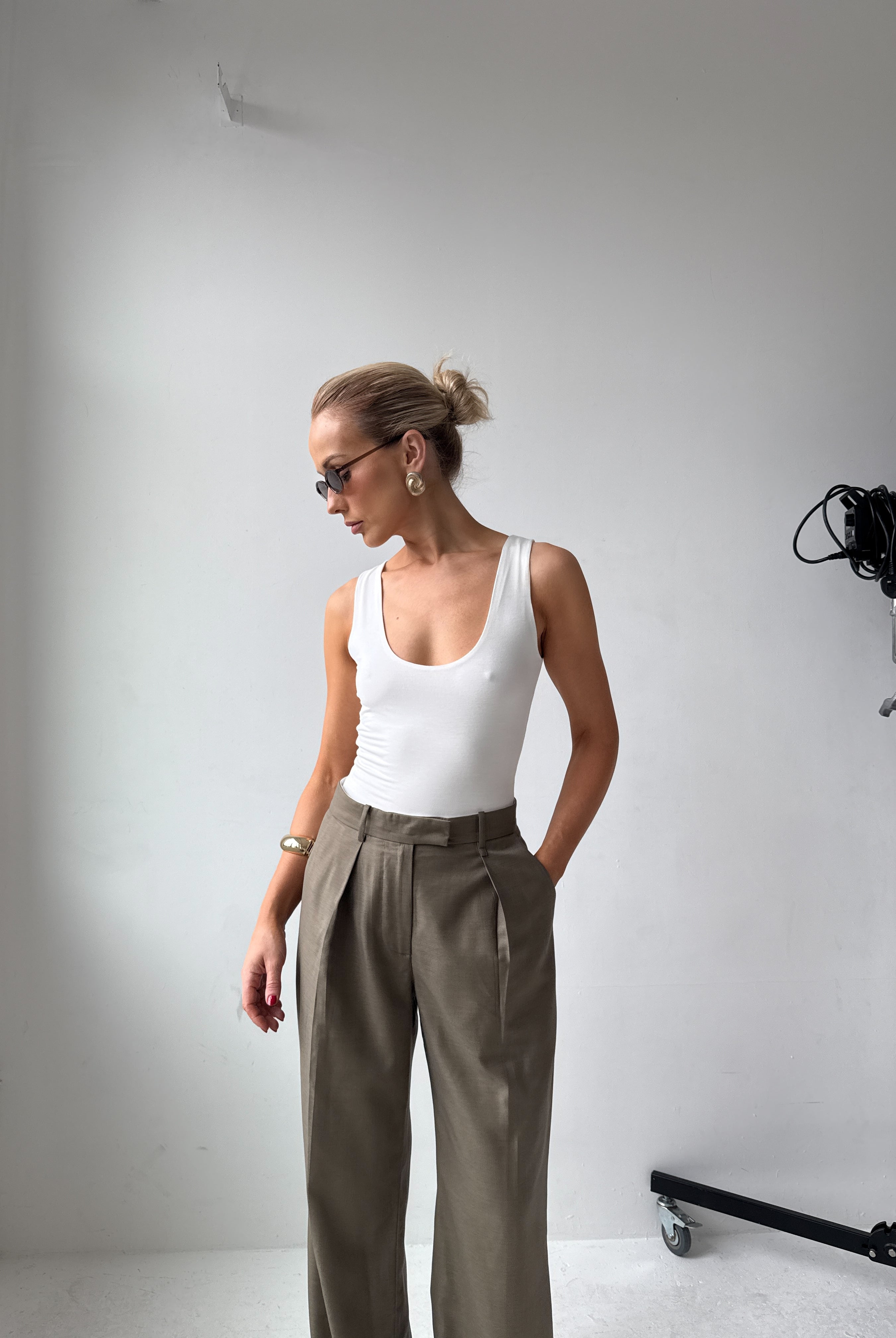 Model in a white tank top and grey trousers standing in a studio setting