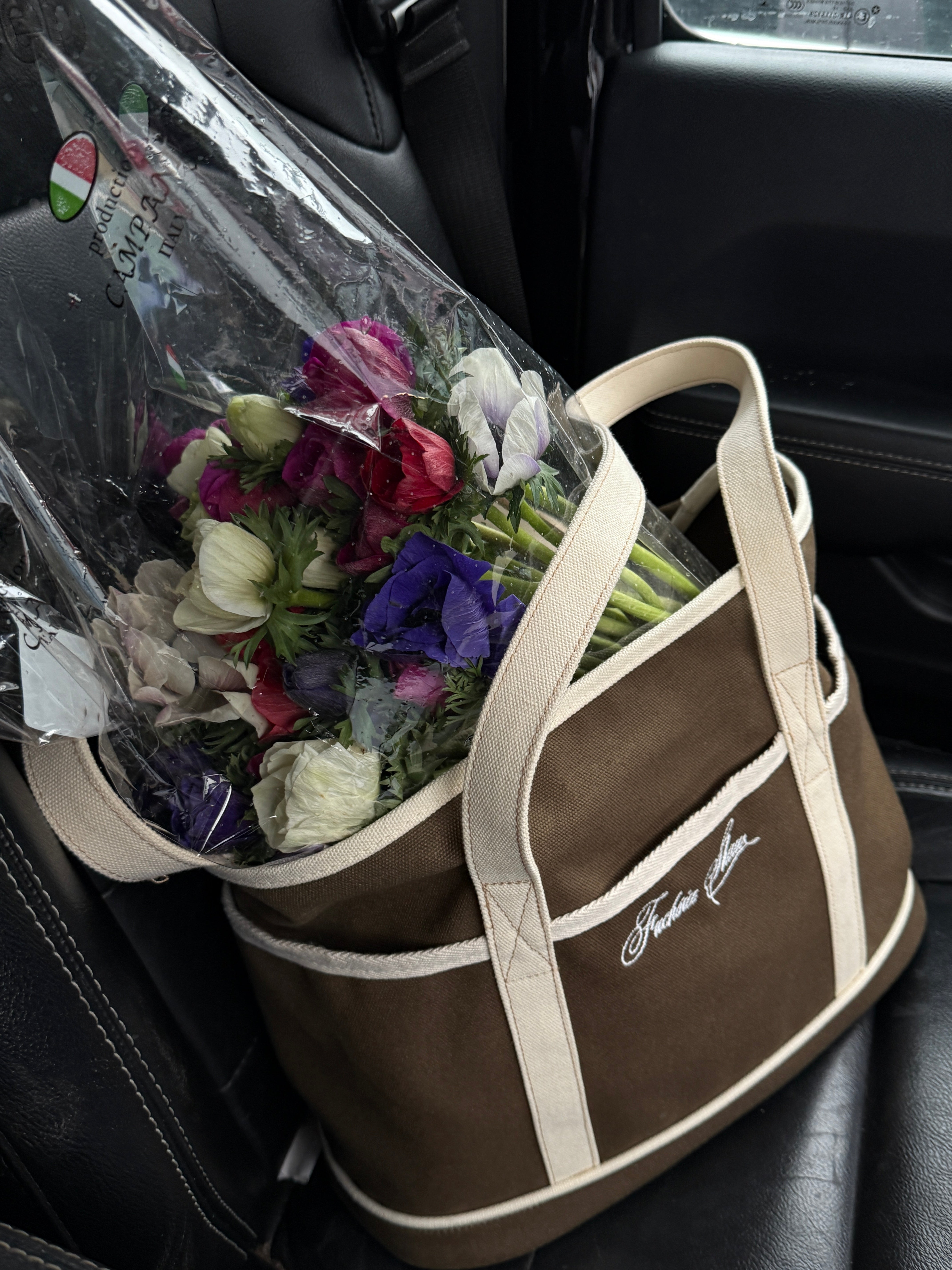 Brown and white tote in the back of a car with a bunch of flowers