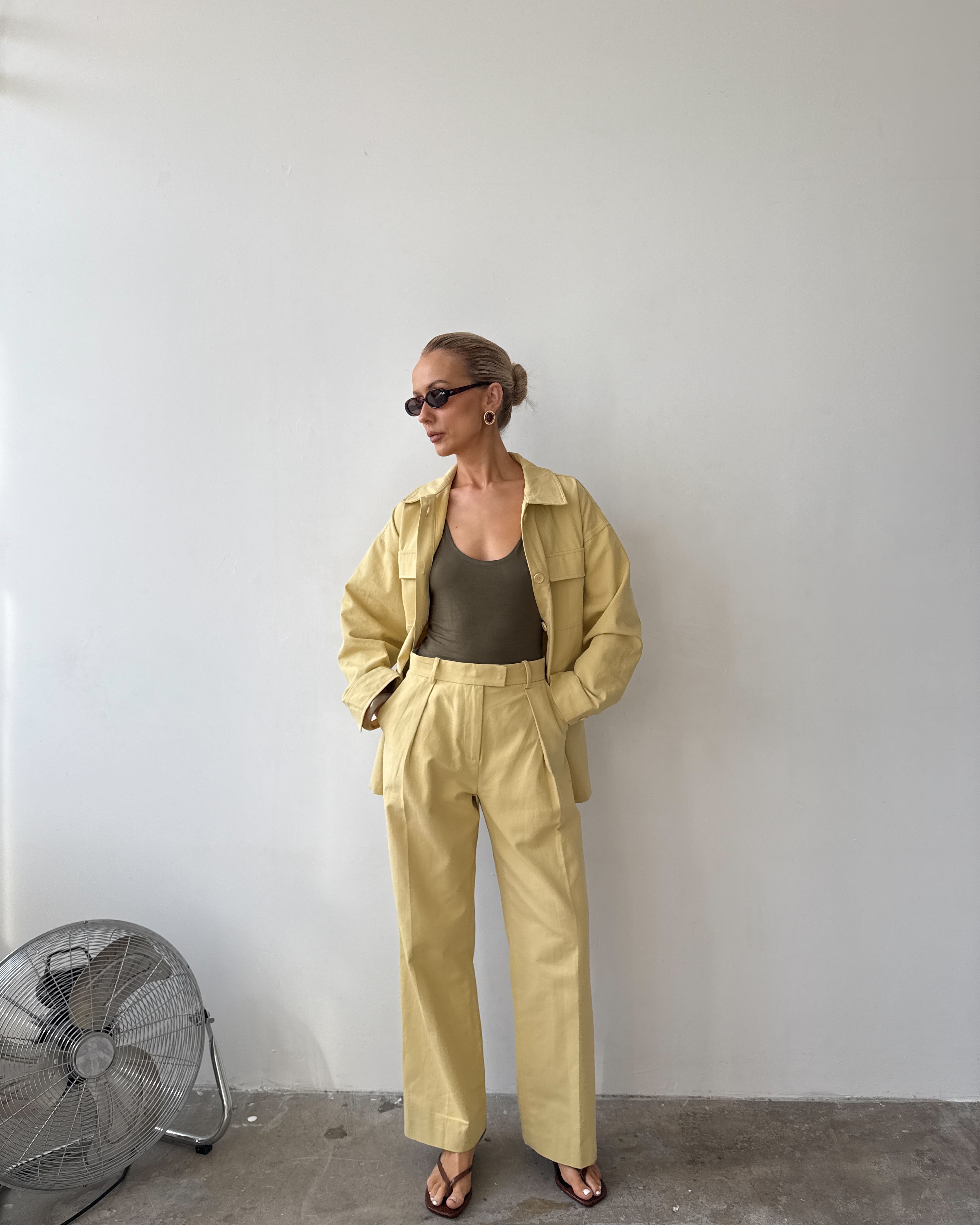 Model wearing a soft yellow jacket with wide sleeves and four front patch pockets, paired with matching trousers, sunglasses and sandals