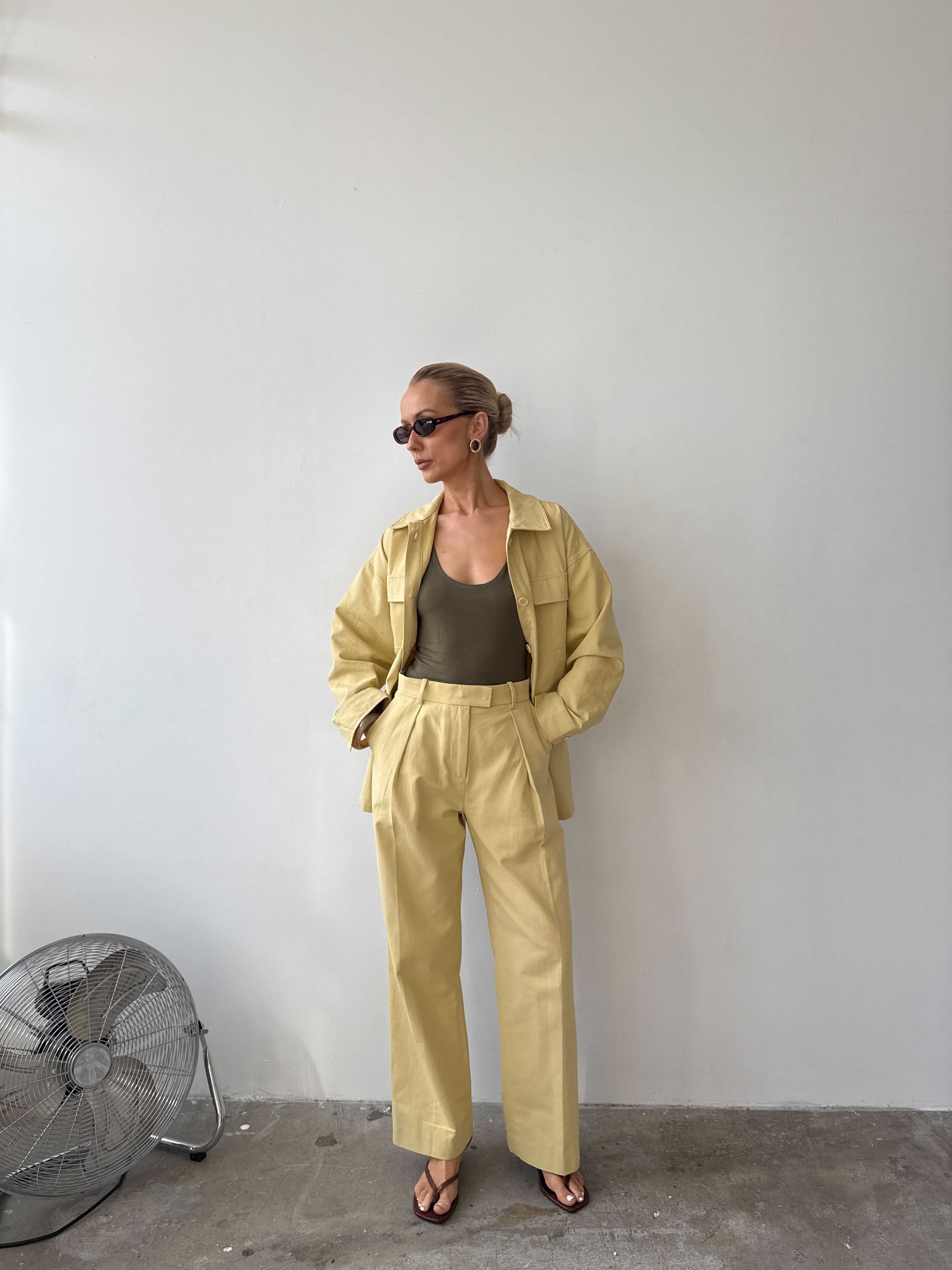 Model wearing a soft yellow jacket with wide sleeves and four front patch pockets, paired with matching trousers, sunglasses and sandals