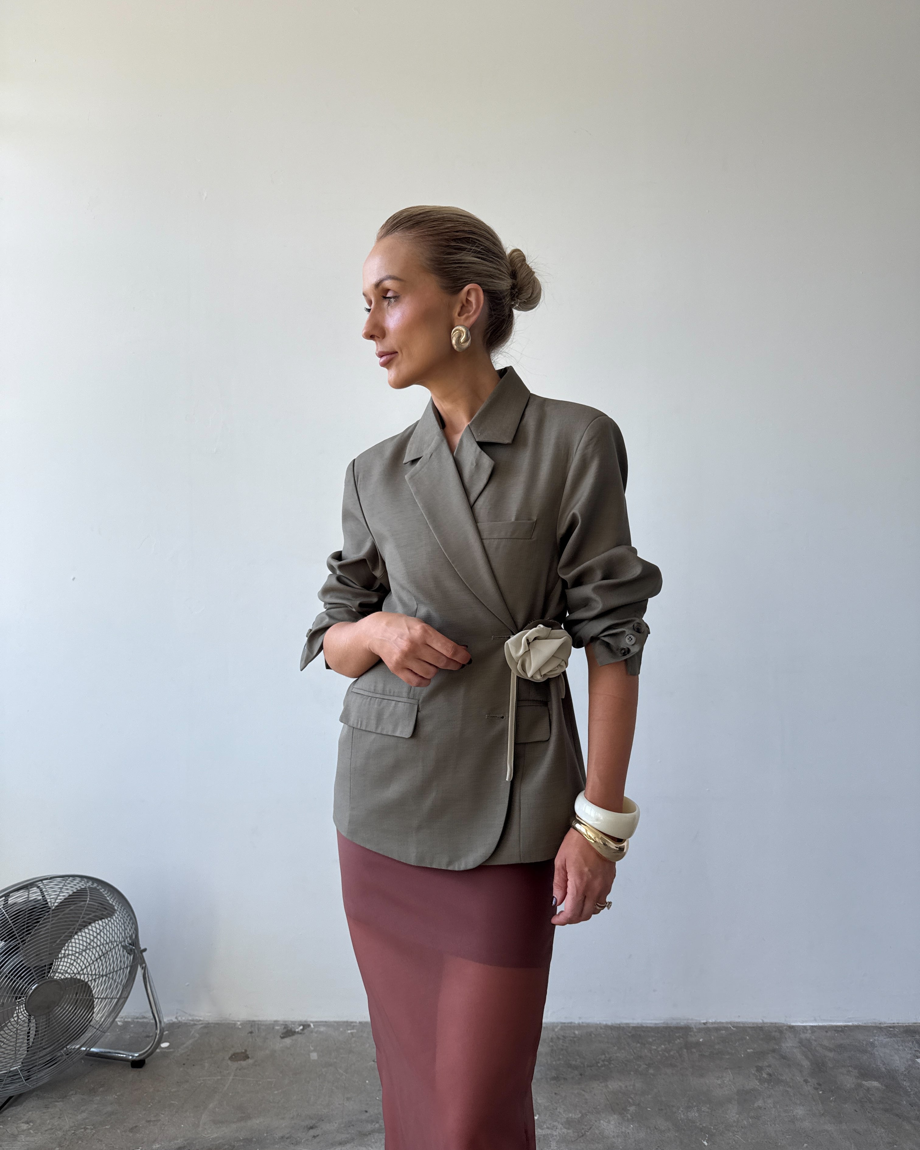 Model is wearing the olive Margaux blazer styled in a wrap-over look with pushed up sleeves paired with the Romée Skirt in Sienna