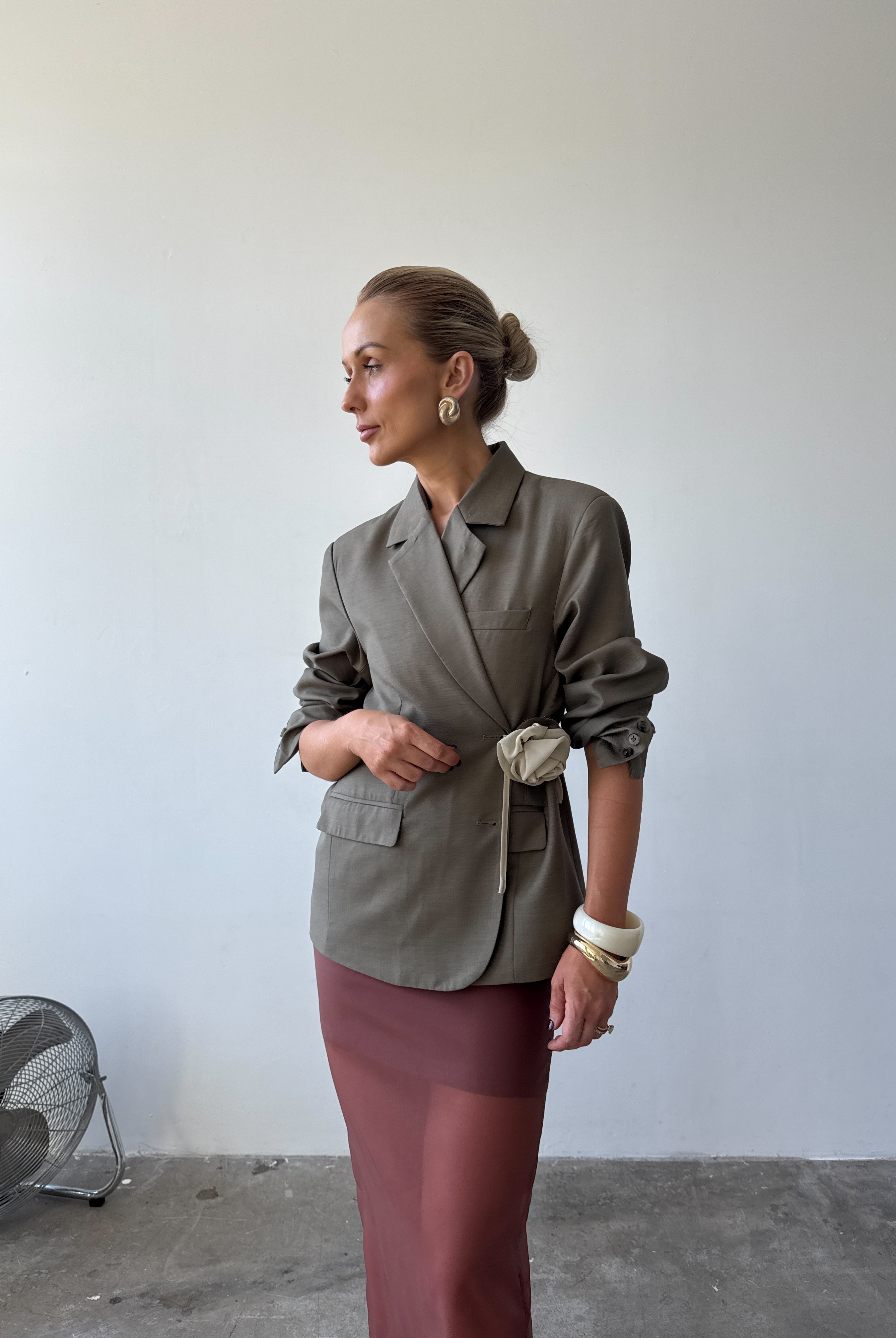 Model is wearing the olive Margaux blazer styled in a wrap-over look with pushed up sleeves paired with the Romée Skirt in Sienna