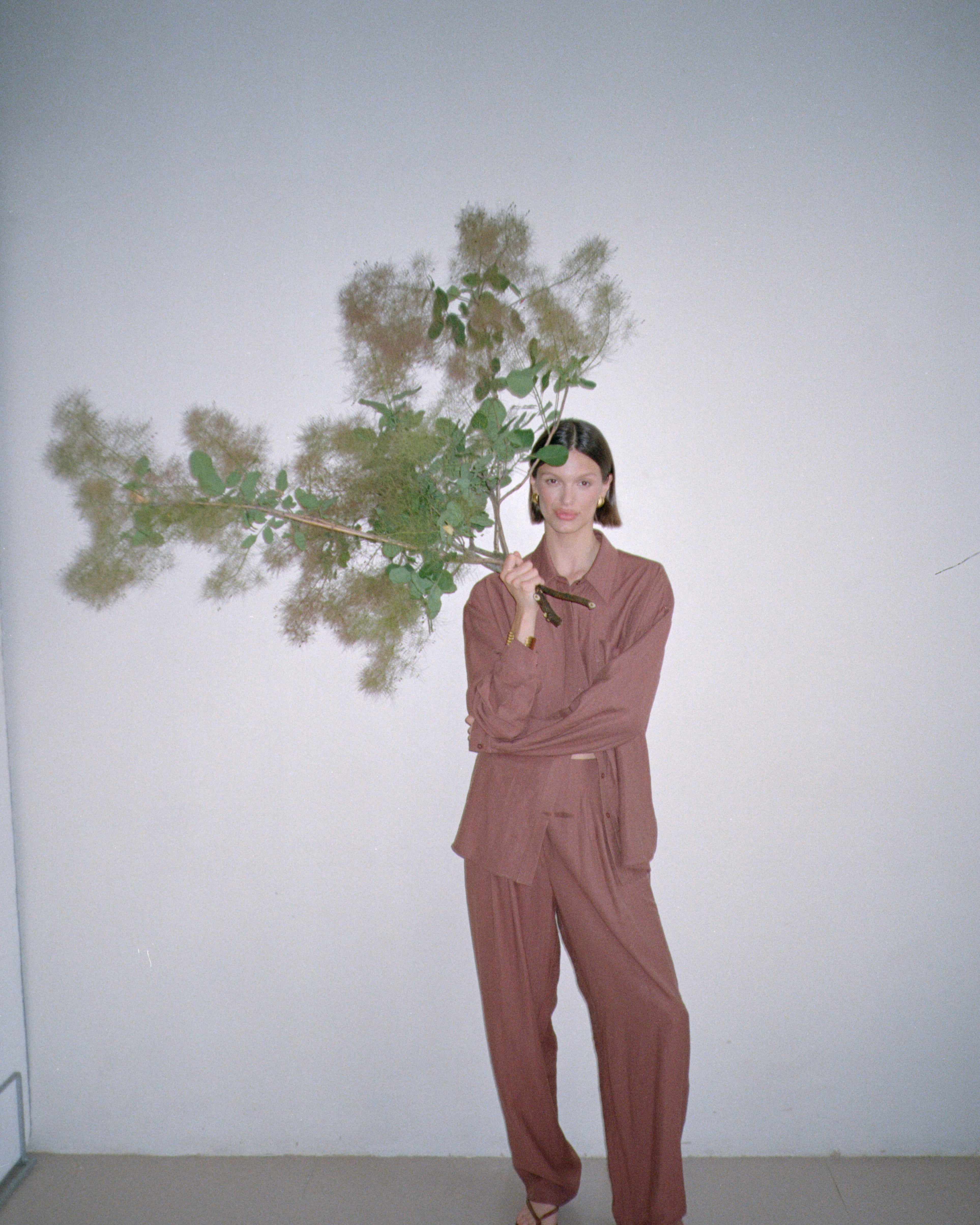 Model wearing a brown outfit standing with large decorative branches in their grasp