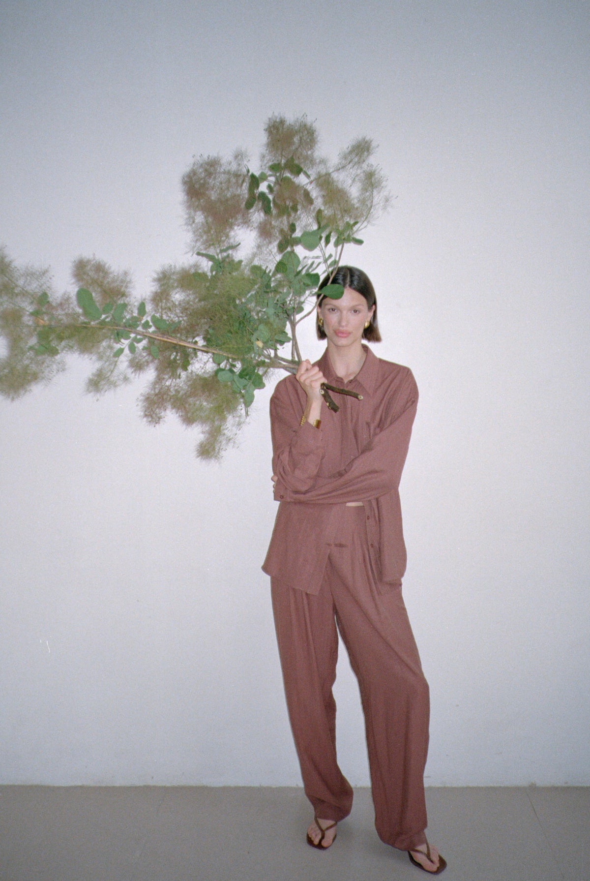 Model wearing a brown outfit standing with large decorative branches in their grasp