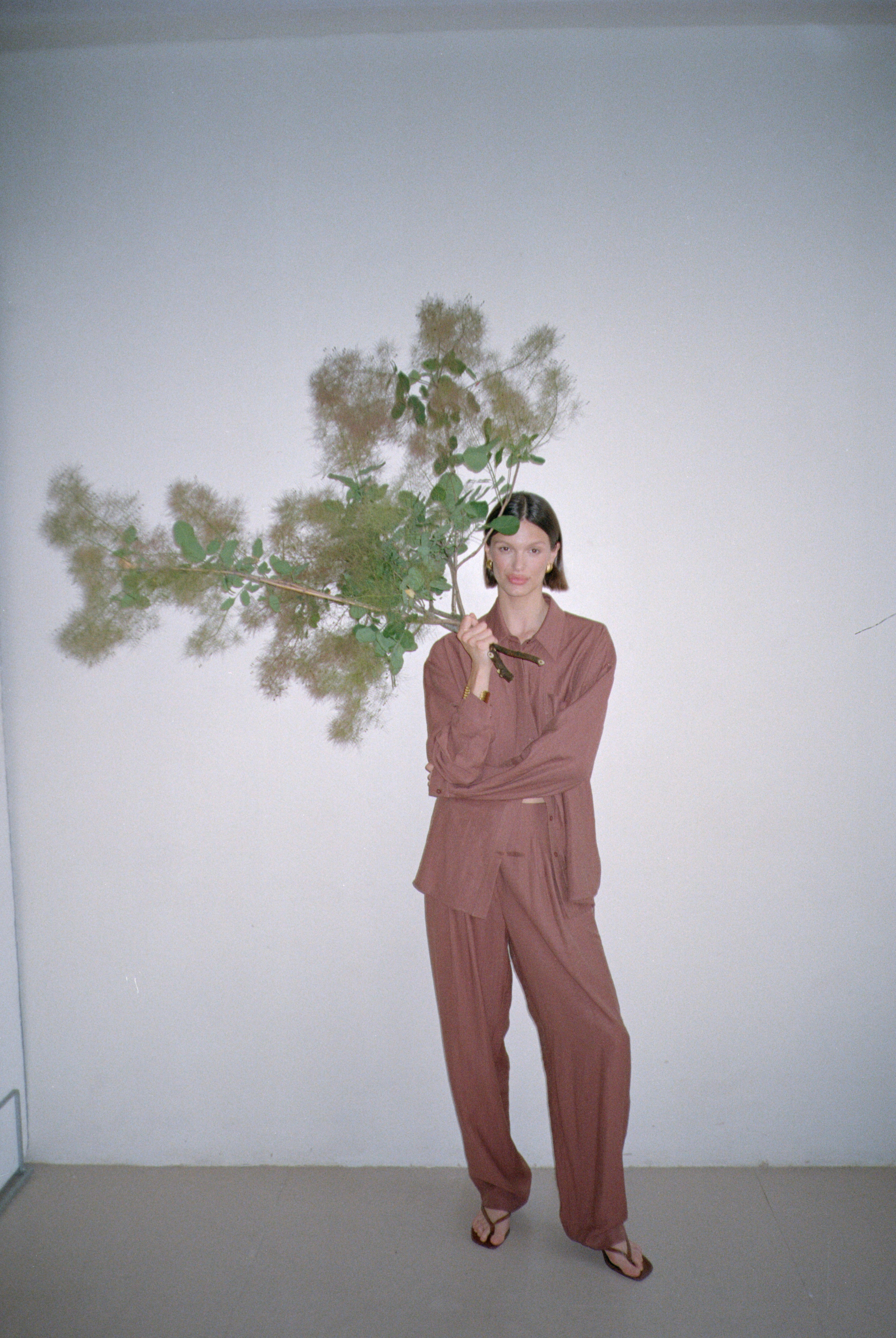 Model wearing a brown outfit standing with large decorative branches in their grasp