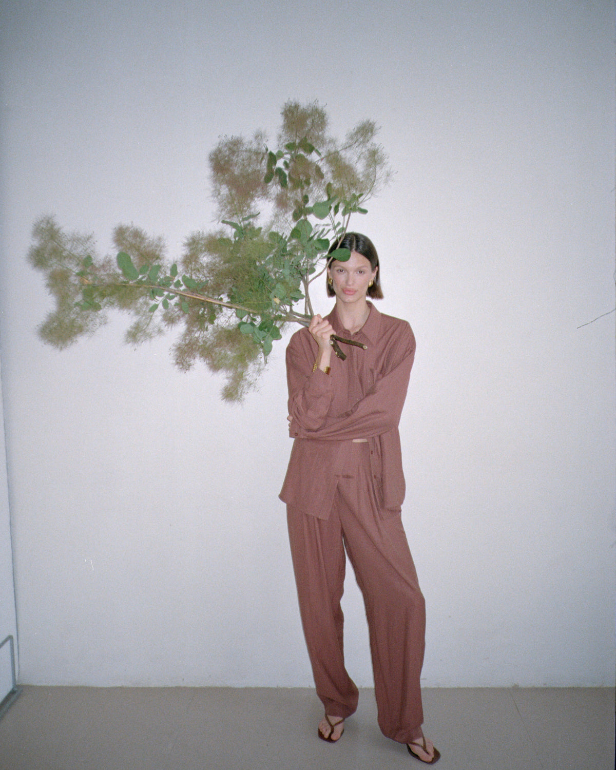 Model wearing a brown outfit standing with large decorative branches in their grasp