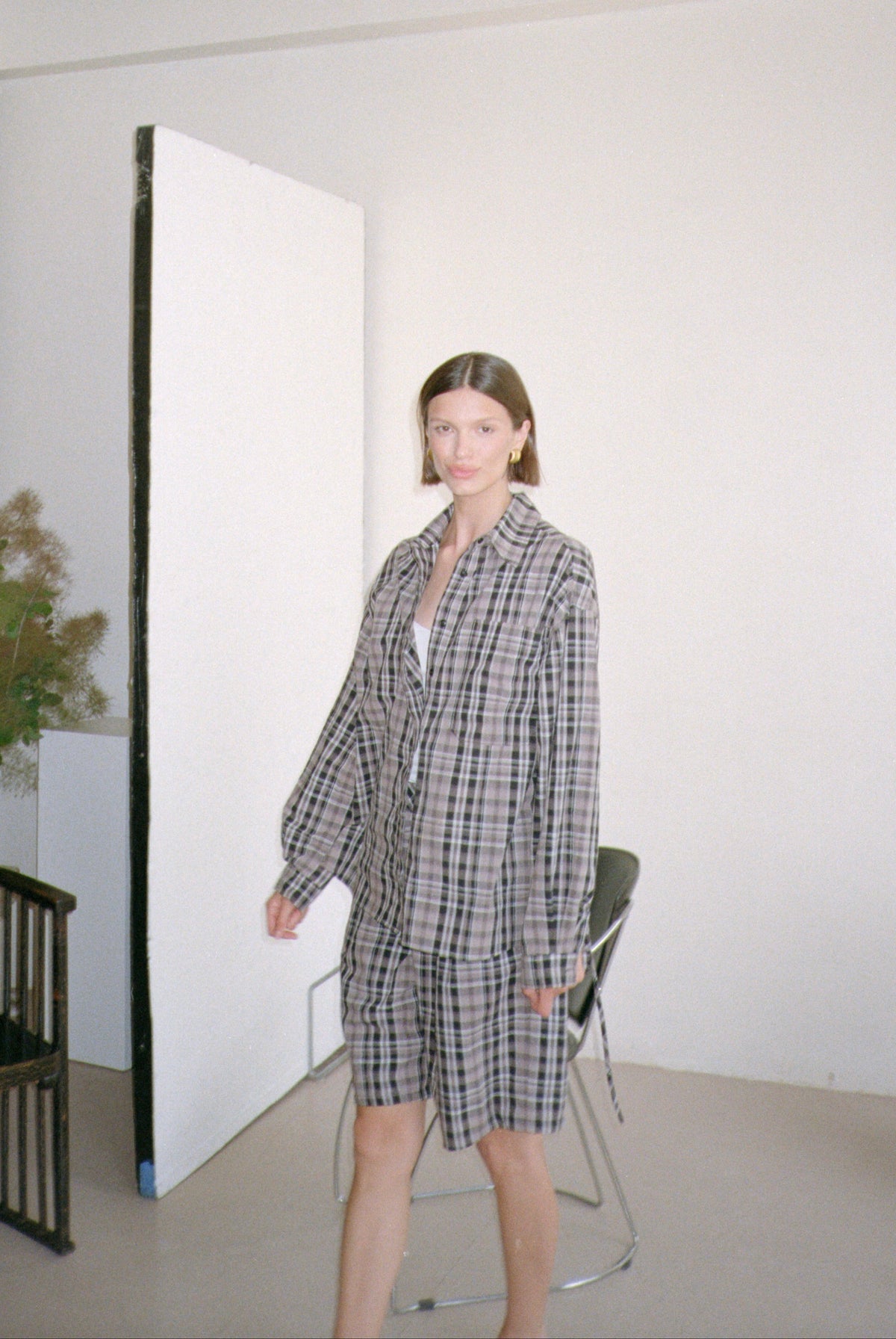 Woman in a checkered outfit standing in a minimalistic room with white walls