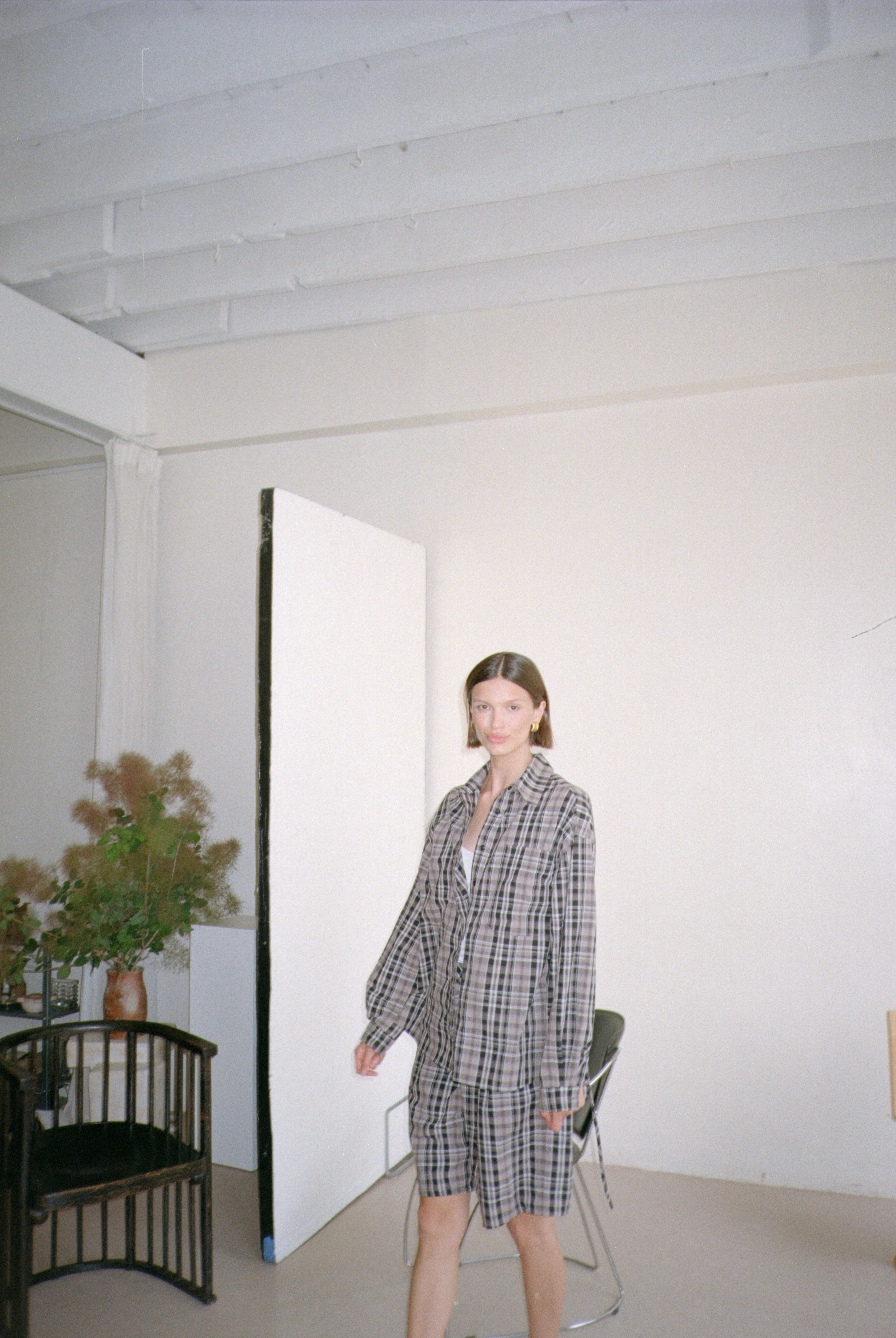 Woman in a checkered outfit standing in a minimalistic room with white walls