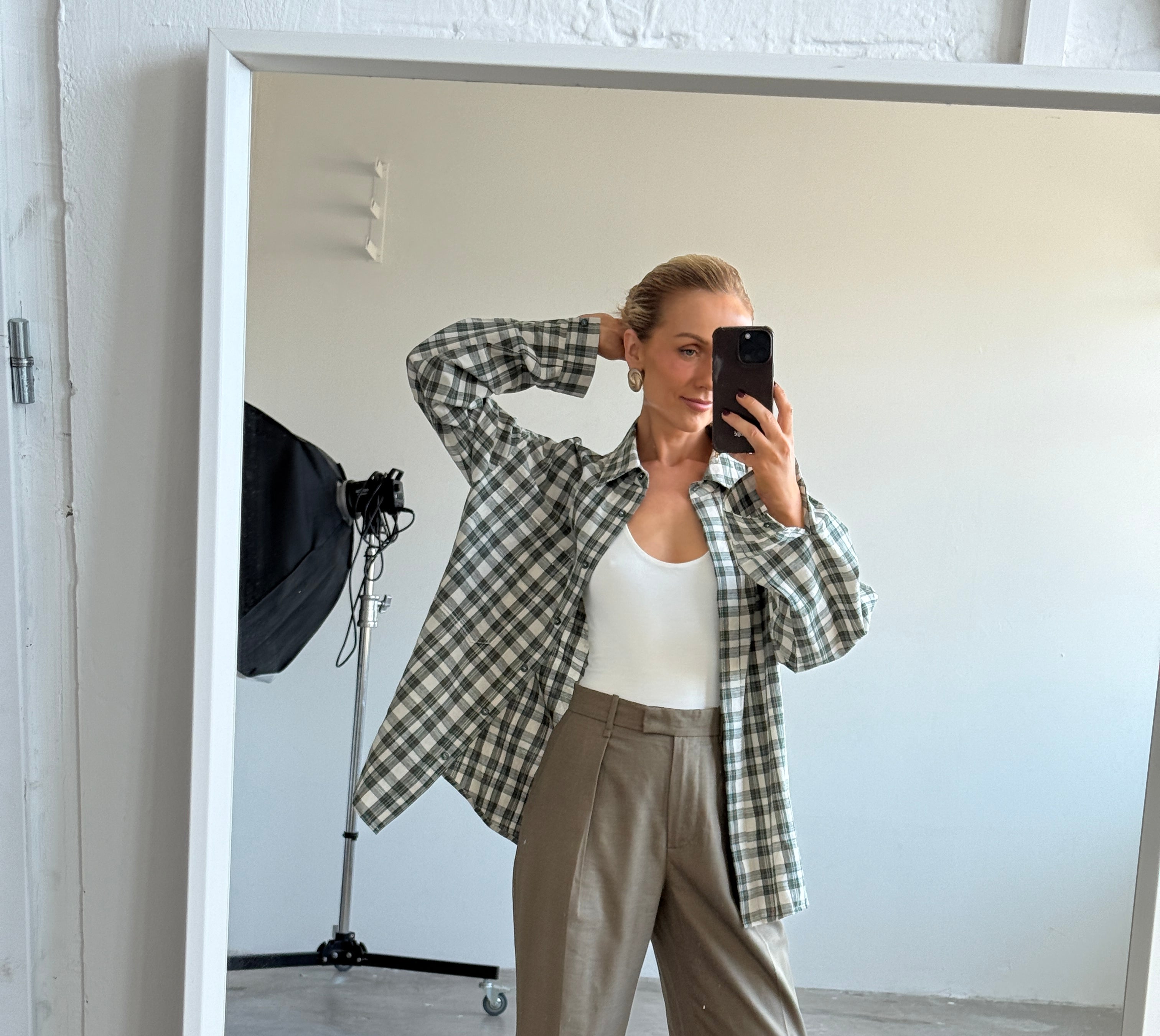 Model taking a mirror selfie wearing a checkered shirt and beige pants