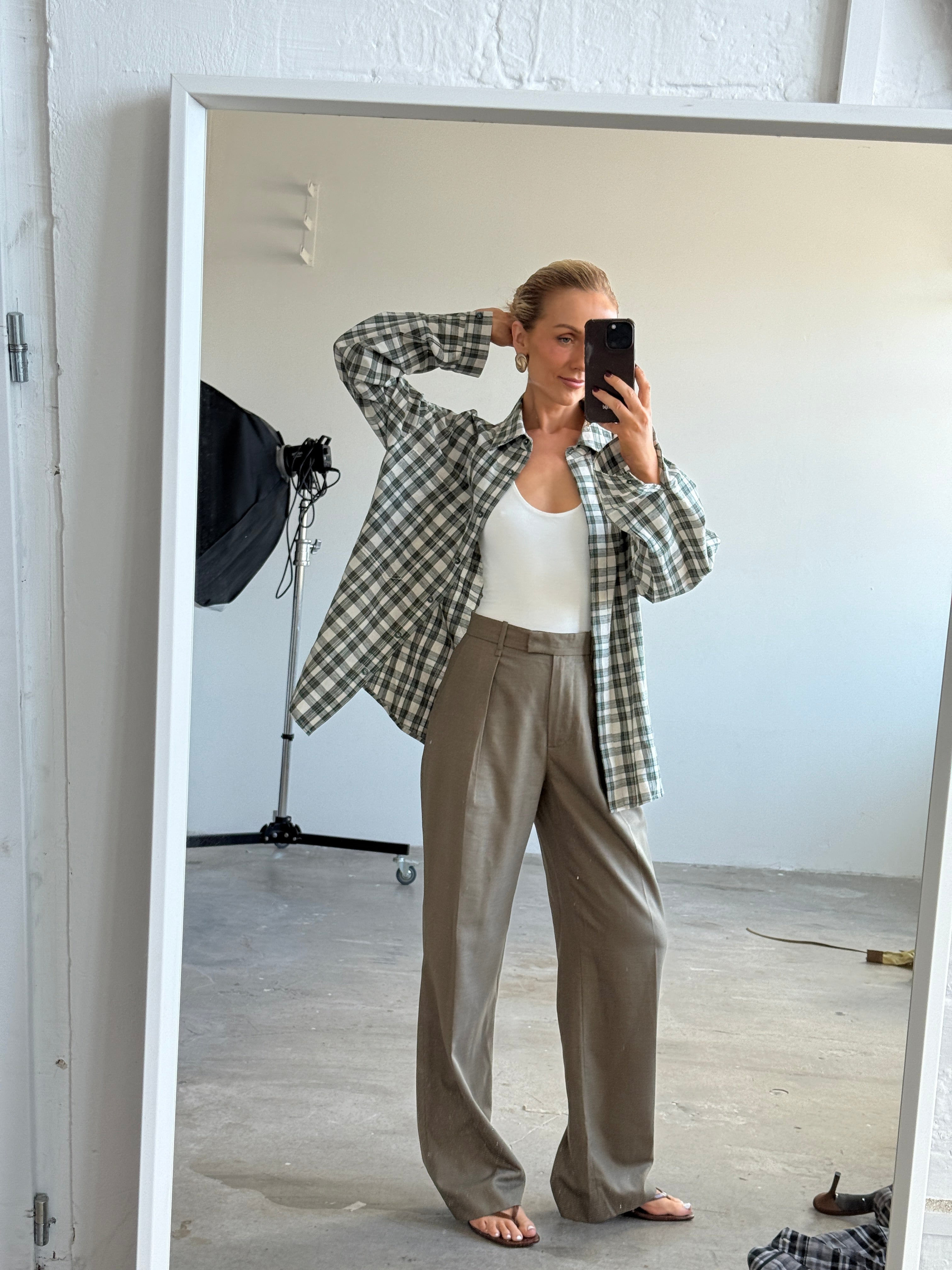 Model taking a mirror selfie wearing a checkered shirt and beige pants