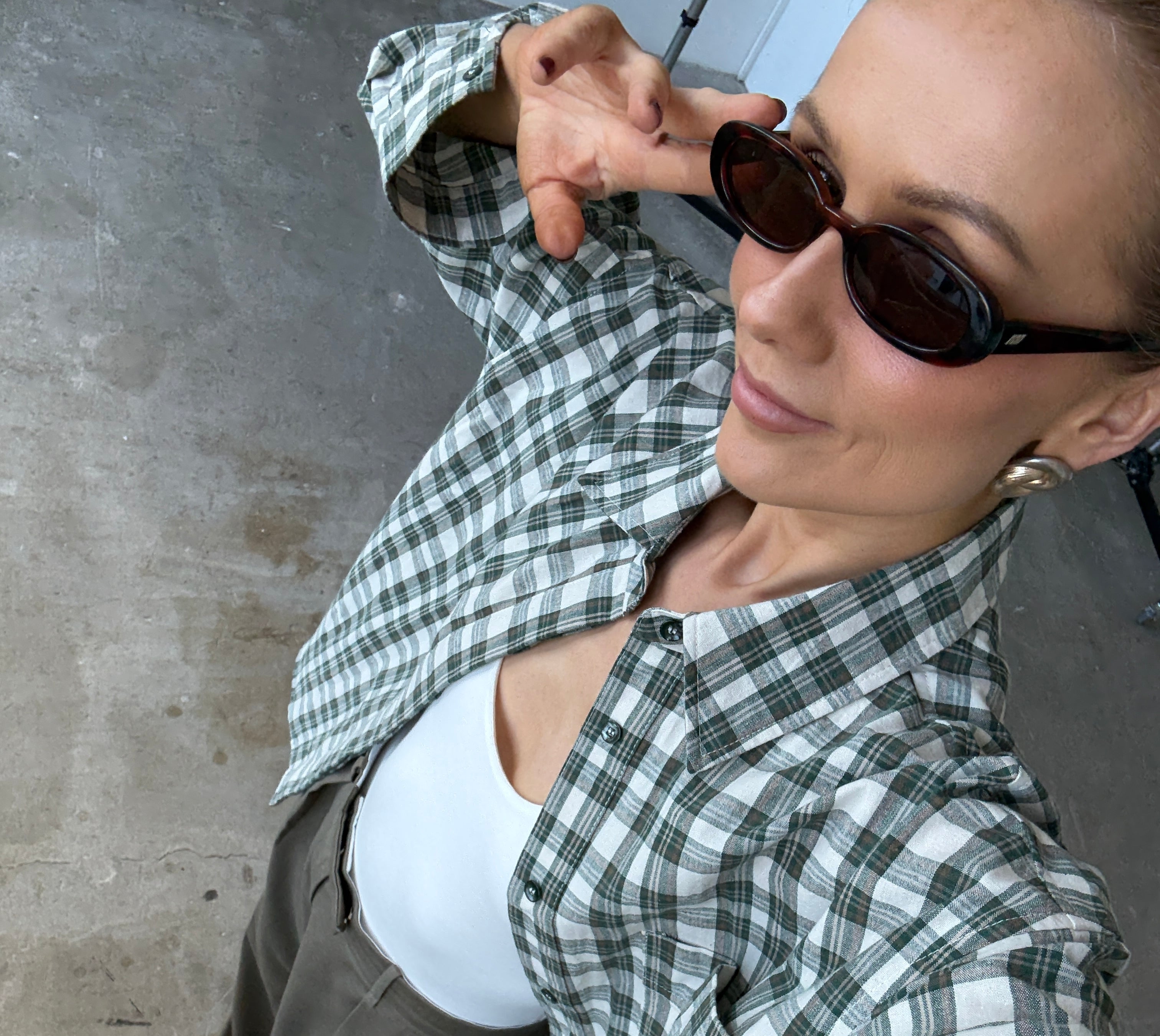Person wearing a green and white checkered shirt with sunglasses on a concrete floor