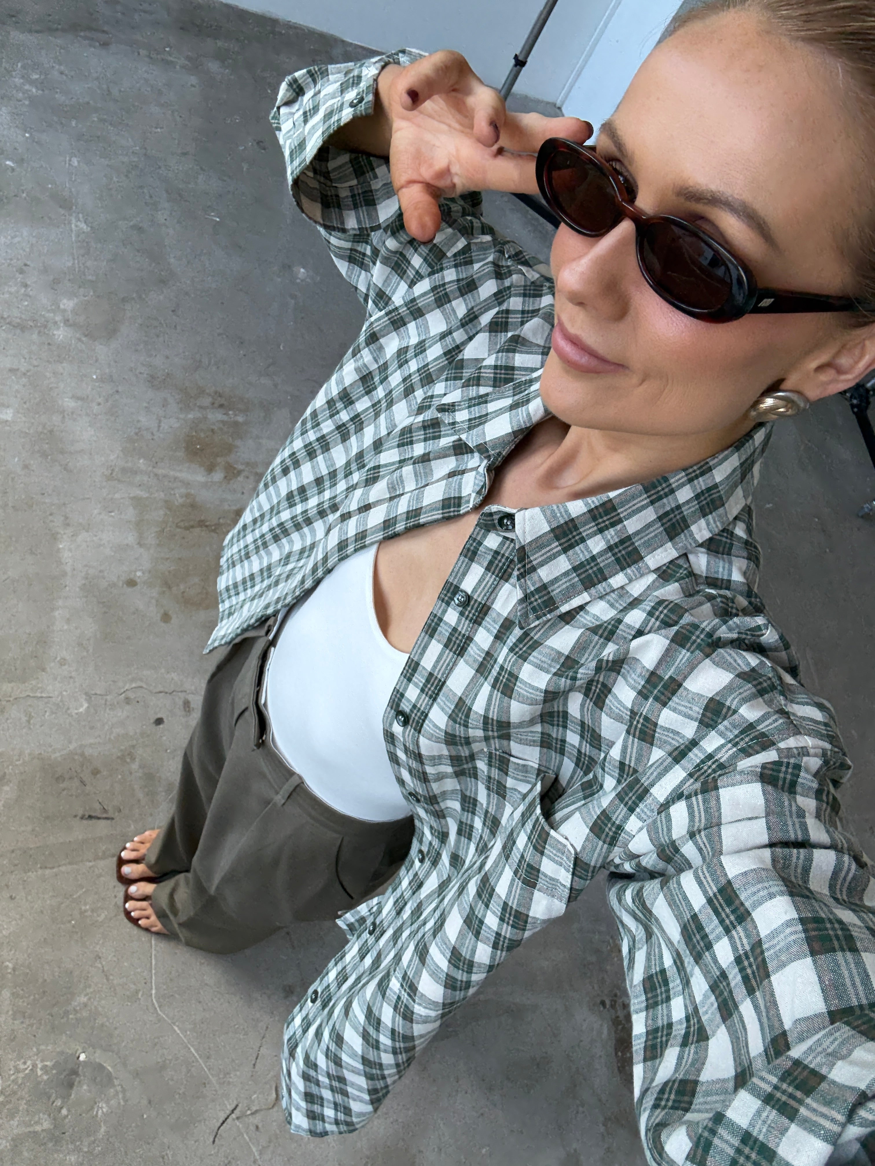 Person wearing a green and white checkered shirt with sunglasses on a concrete floor