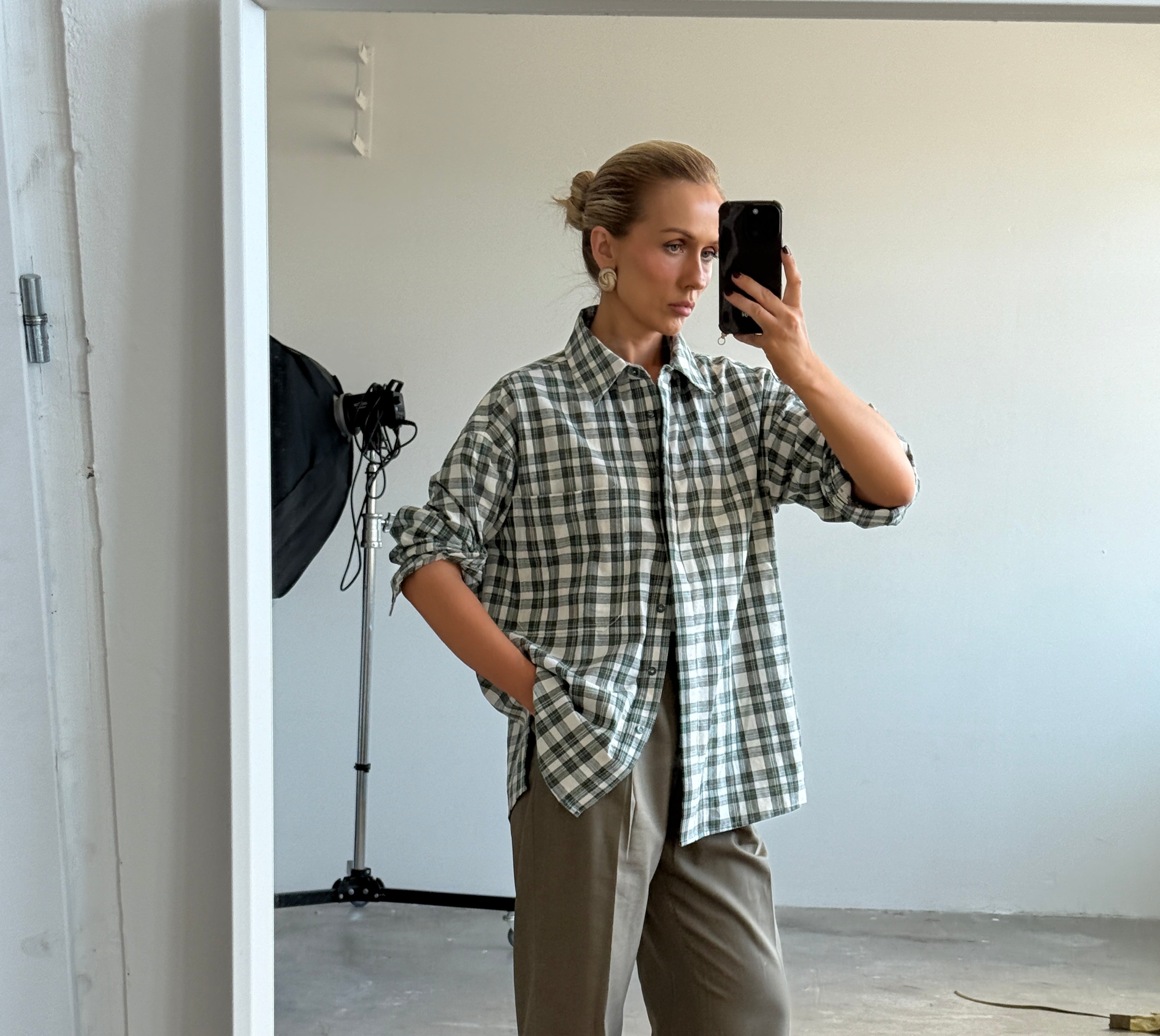 Model taking a mirror selfie wearing a checkered shirt and slate grey trousers
