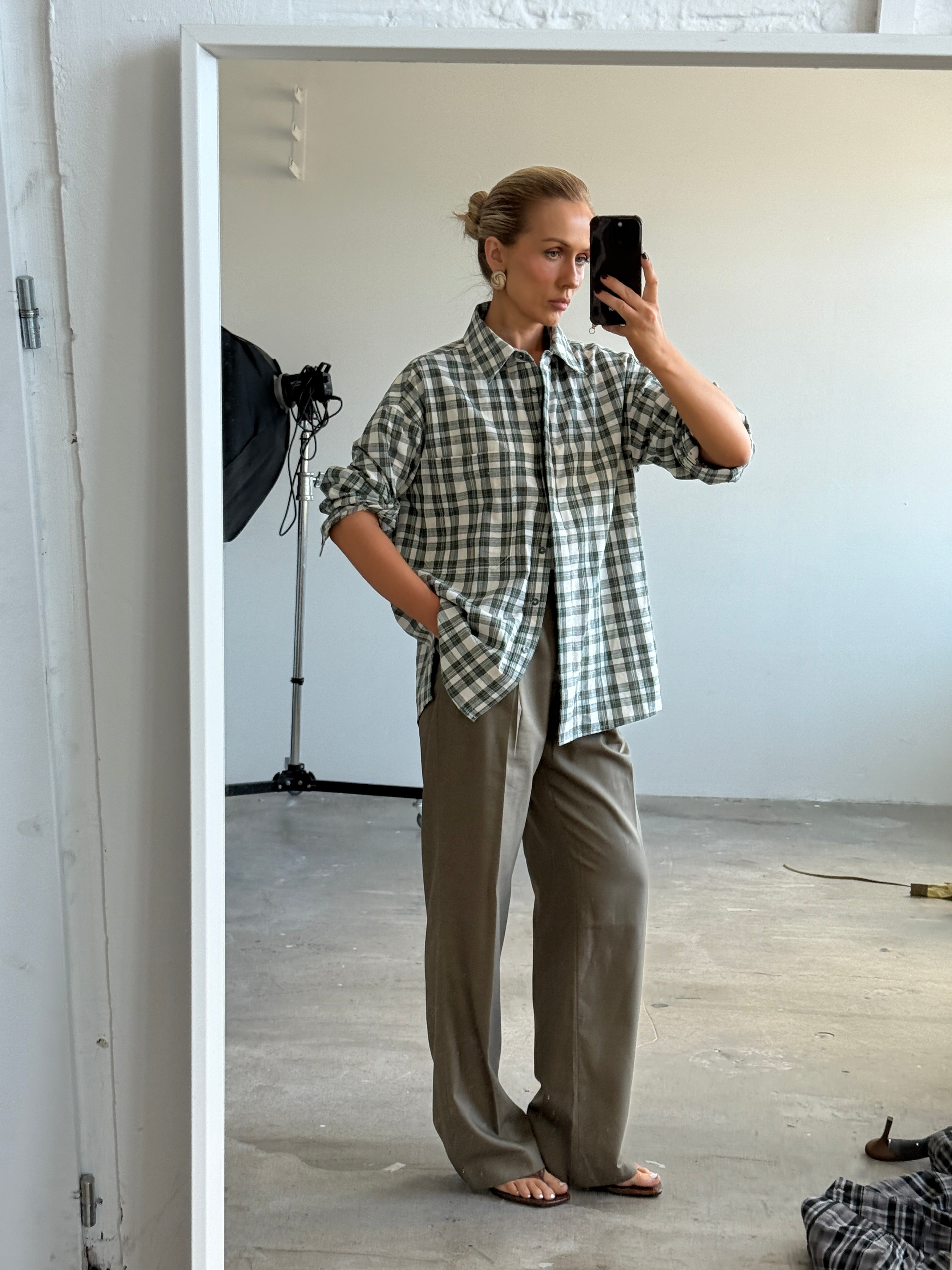 Model taking a mirror selfie wearing a checkered shirt and slate grey trousers