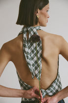 Woman wearing a green plaid top with a flower, against a plain background