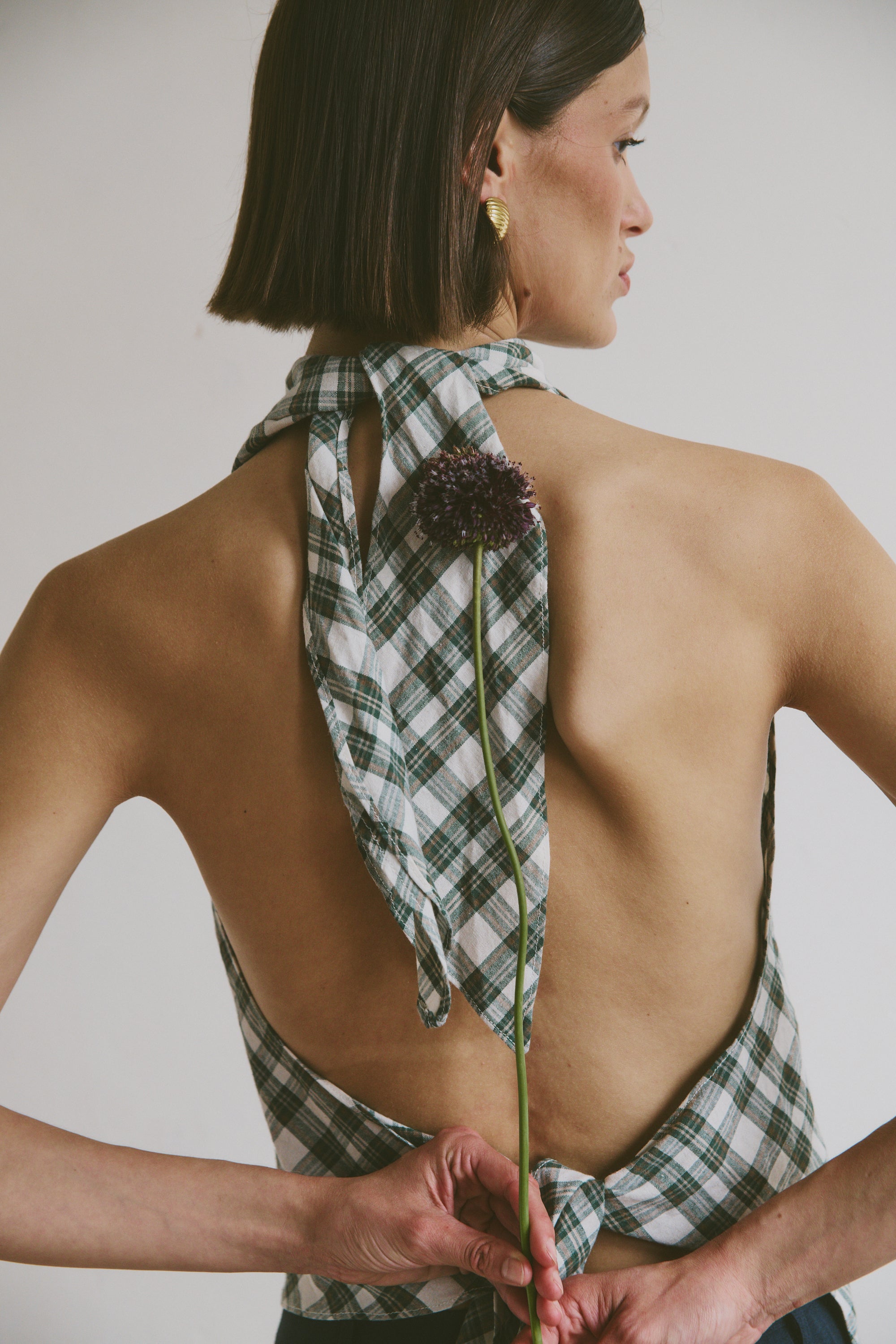 Woman wearing a green plaid top with a flower, against a plain background