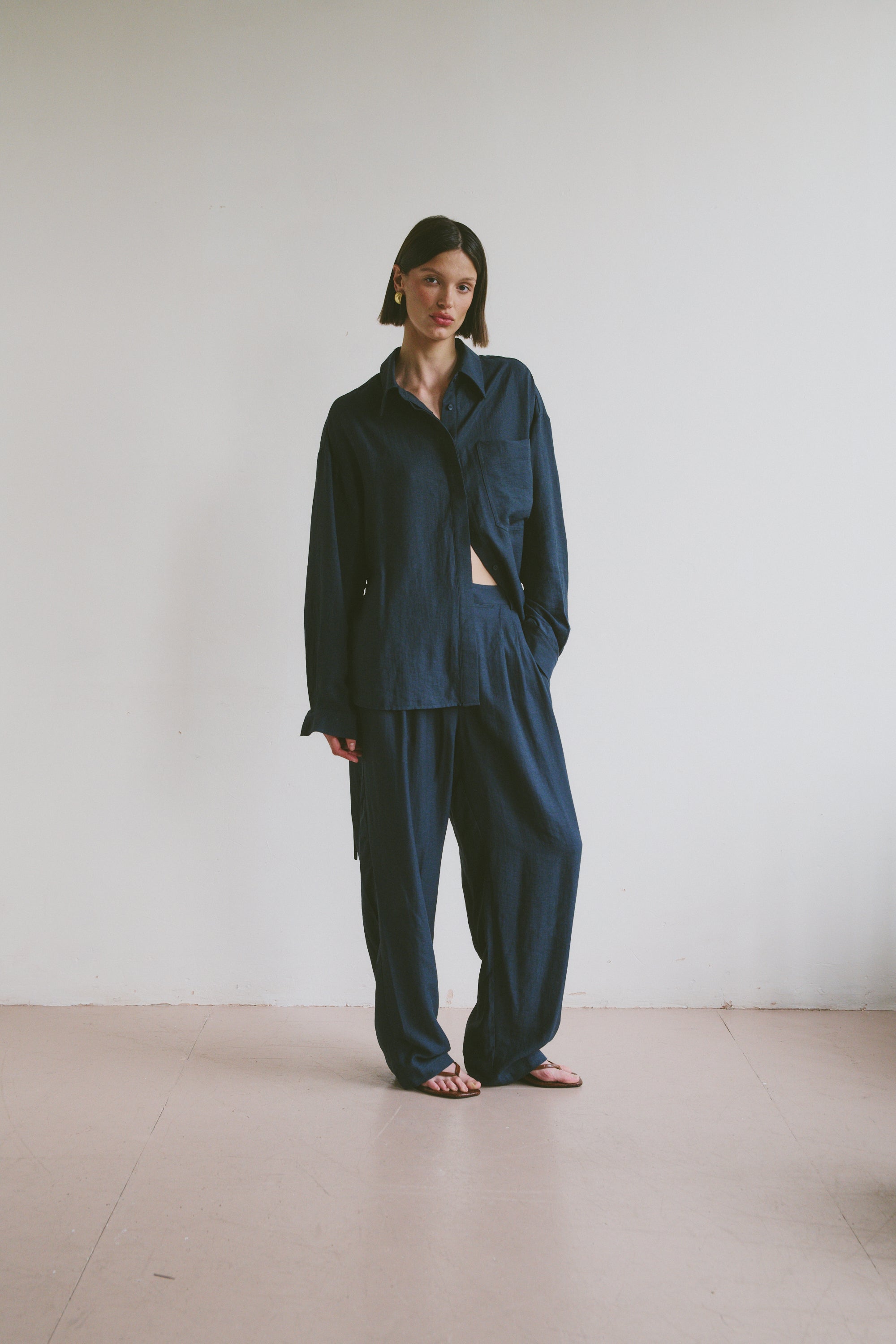 Model wearing a relaxed dark blue outfit standing against a plain white wall.