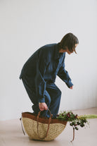 Model in blue outfit with a woven basket and flowers on a light background